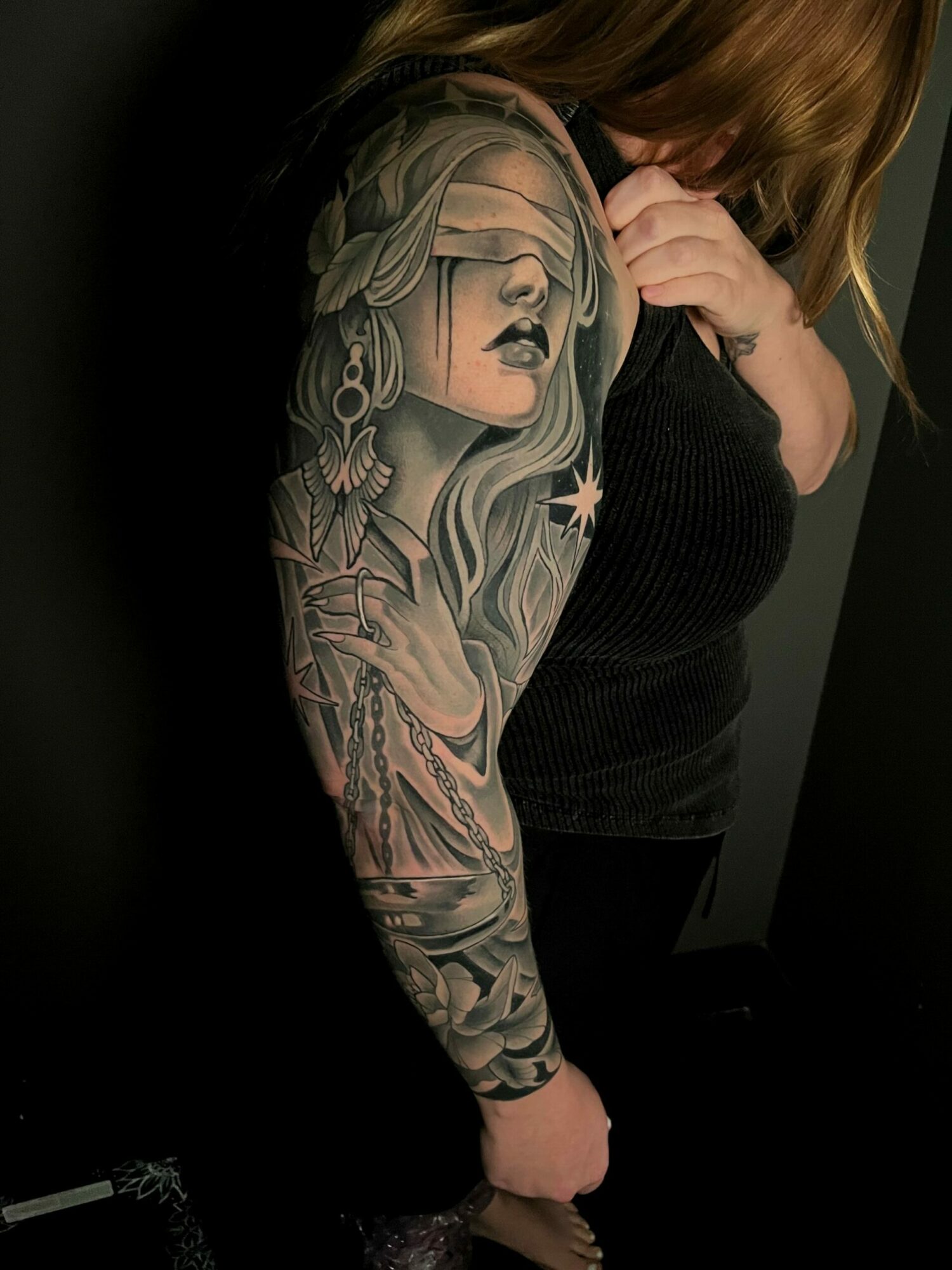 Person lying down with a detailed tattoo sleeve on their arm, resting their head on their hand, dark background.