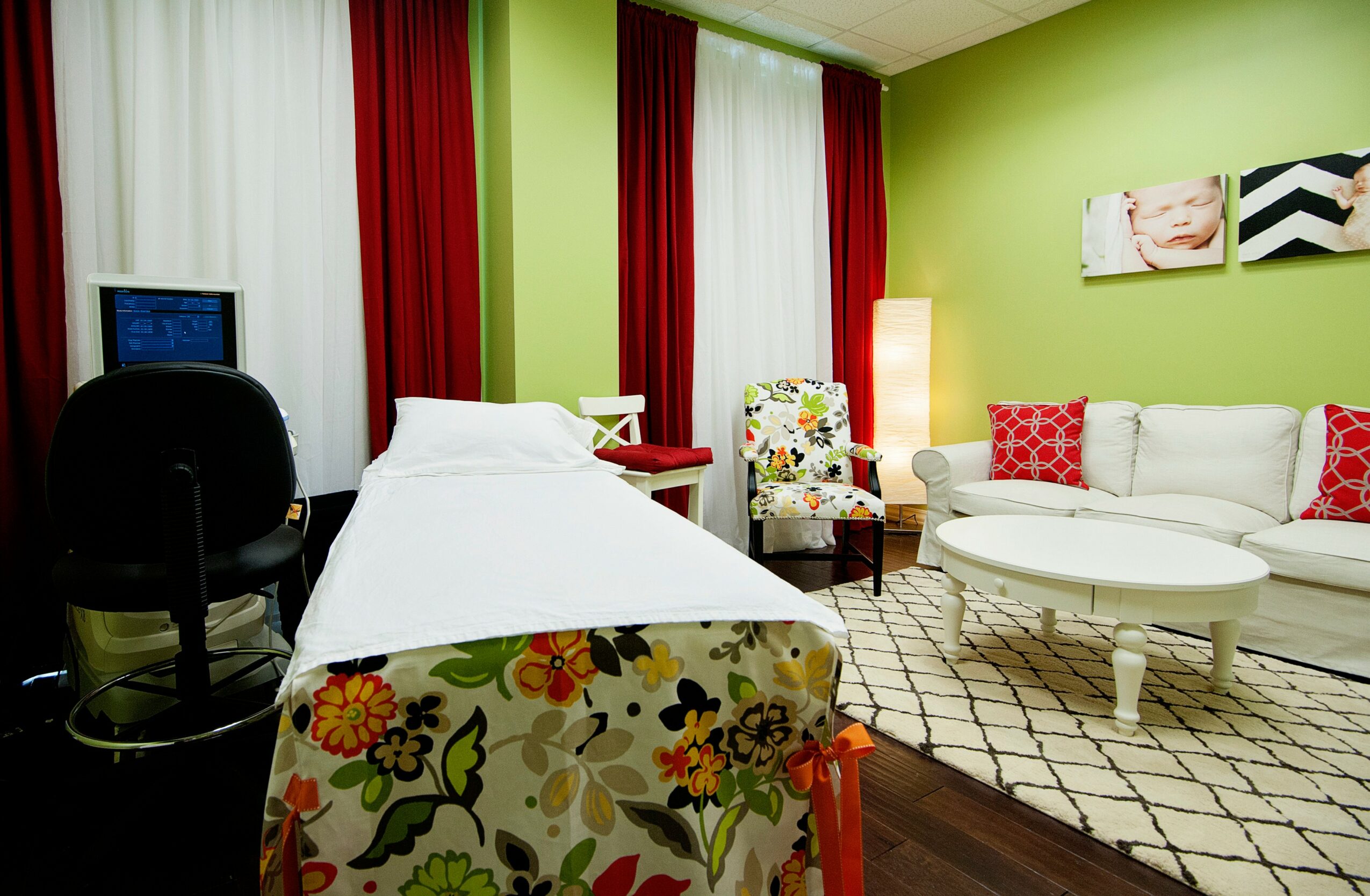Room with a bed, armchair, sofa, and a small table, green walls, red curtains, and wall art, with a patterned bedspread.