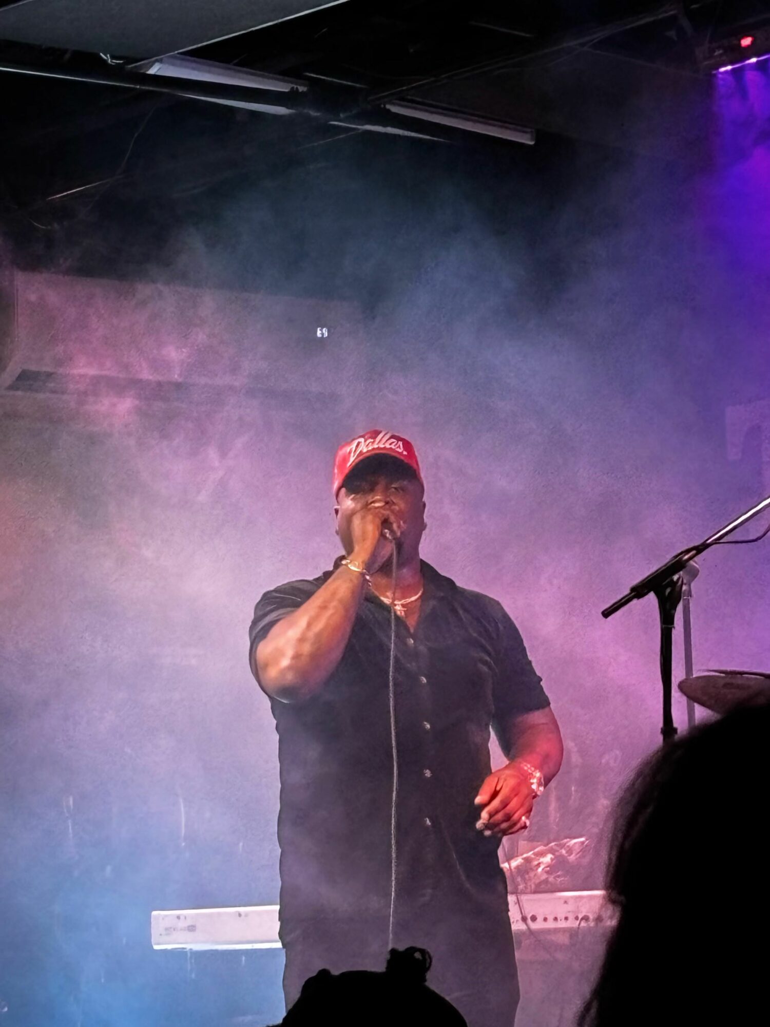 Person singing into microphone on stage with colorful lighting and smoke effects.