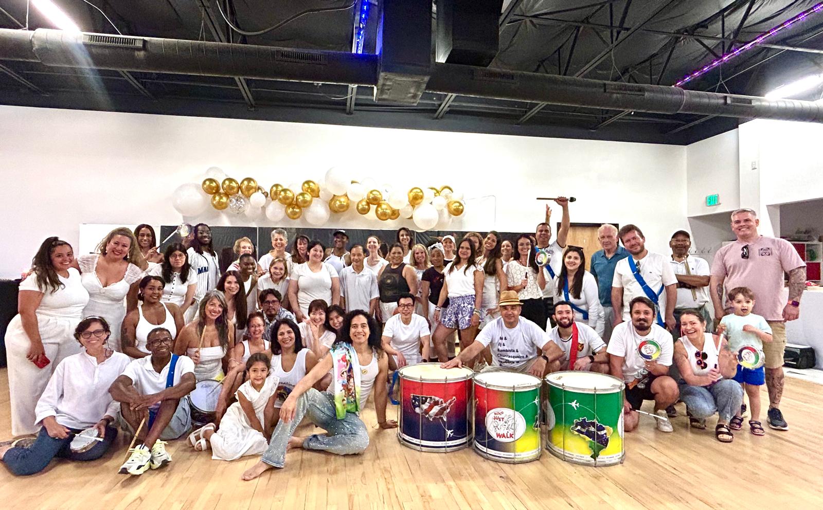 Group of people posing indoors with musical instruments and decorations, some sitting and some standing, in a spacious room.