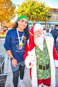 Young woman wearing a green headband and blue sweatshirt standing next to Santa Claus in a festive outdoor setting.