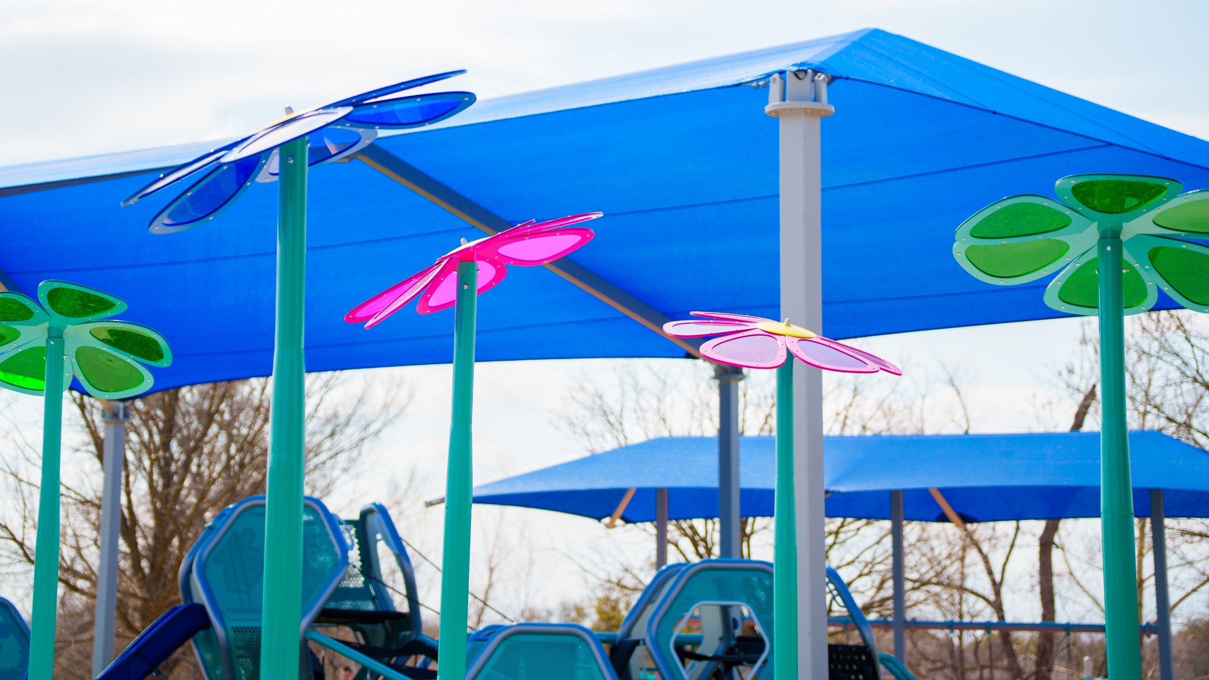 Colorful umbrellas and shade structures at a playground or park area, with trees in the background.