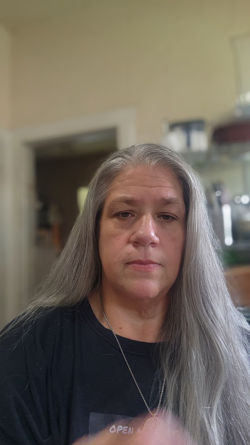 Woman with long gray hair looking at the camera in an indoor setting.