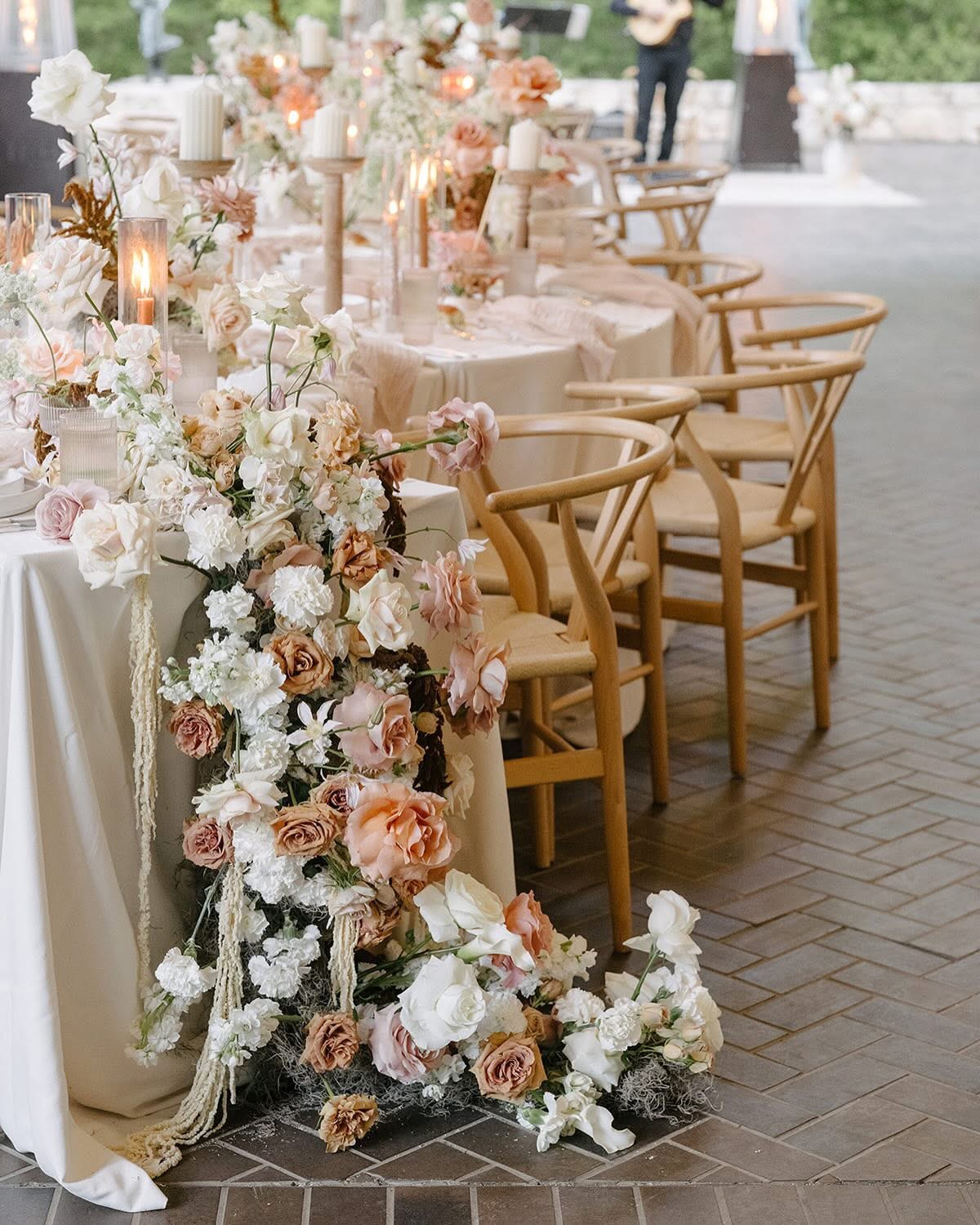 Elegant outdoor table setting with floral arrangements and wooden chairs, ready for a celebration or event.