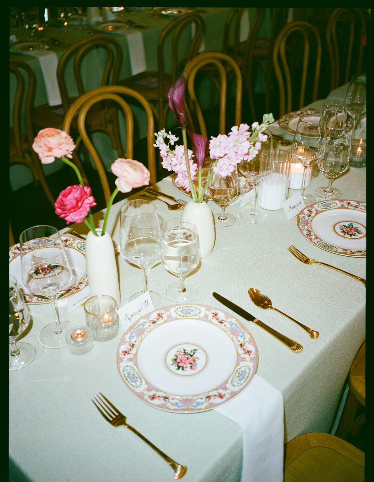 Elegant table setting with floral centerpieces, plates, glasses, and gold utensils on a white tablecloth.