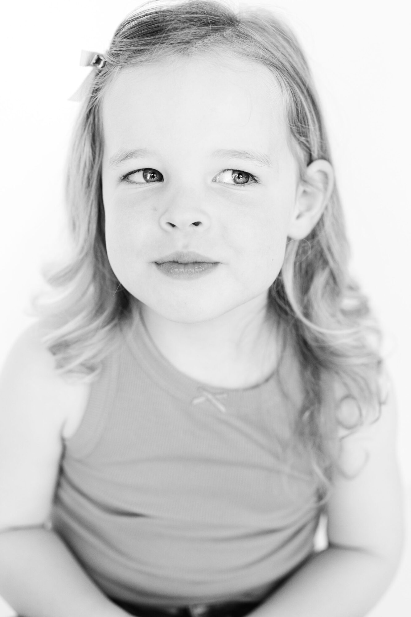 Young girl with wavy hair looking to the side, wearing a sleeveless top, in black and white.