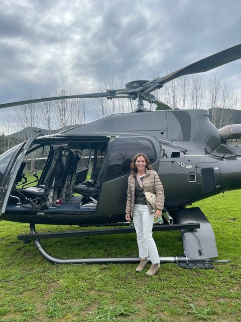 Person standing next to a helicopter on grass, cloudy sky in background.