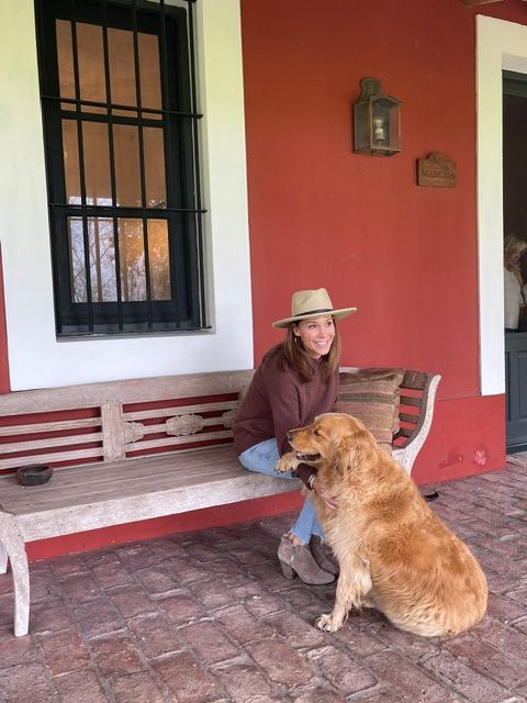 Person sitting on a bench with a dog, in front of a red wall and window with bars.
