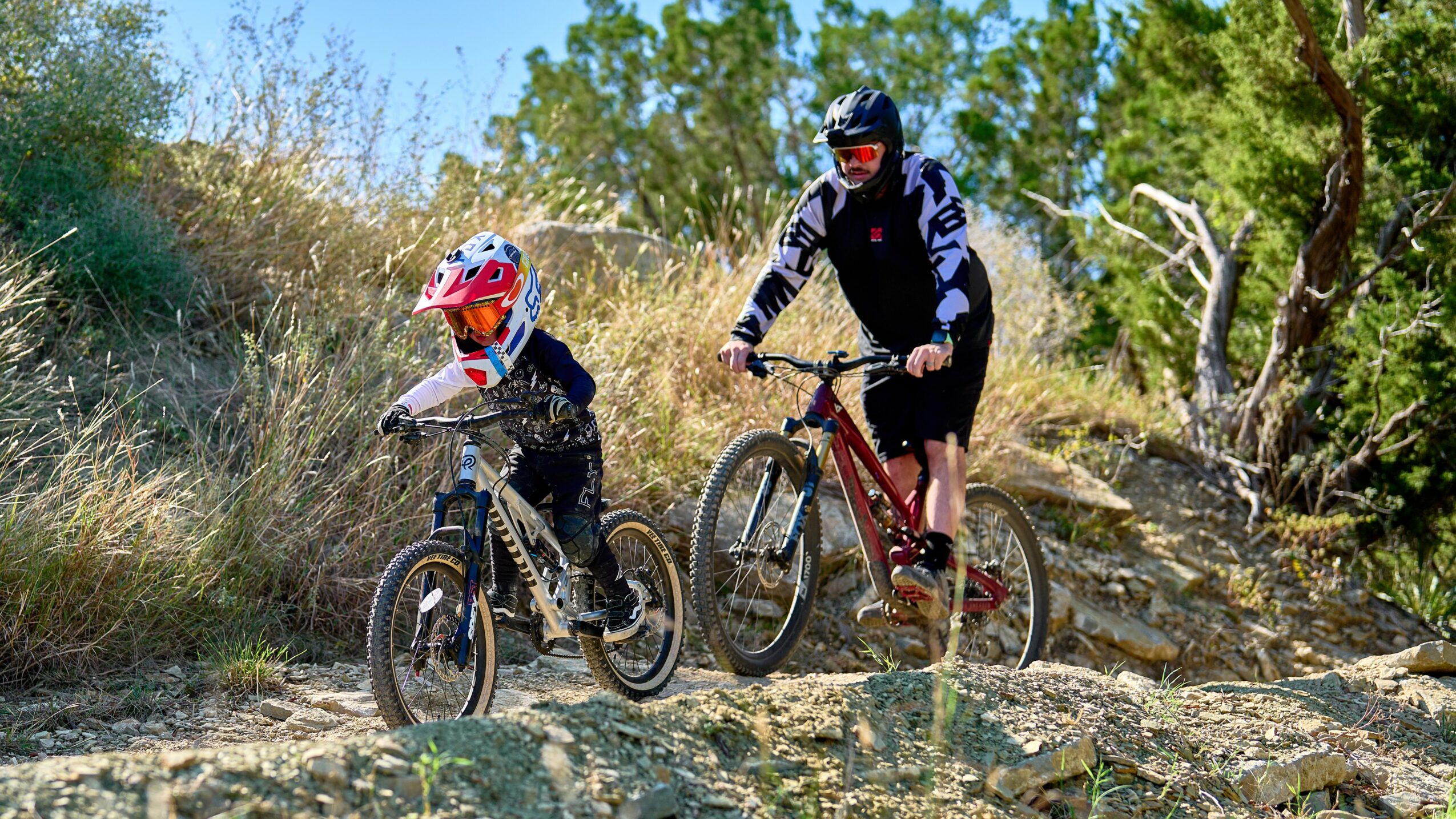 Two people riding mountain bikes on a dirt trail surrounded by trees and bushes.