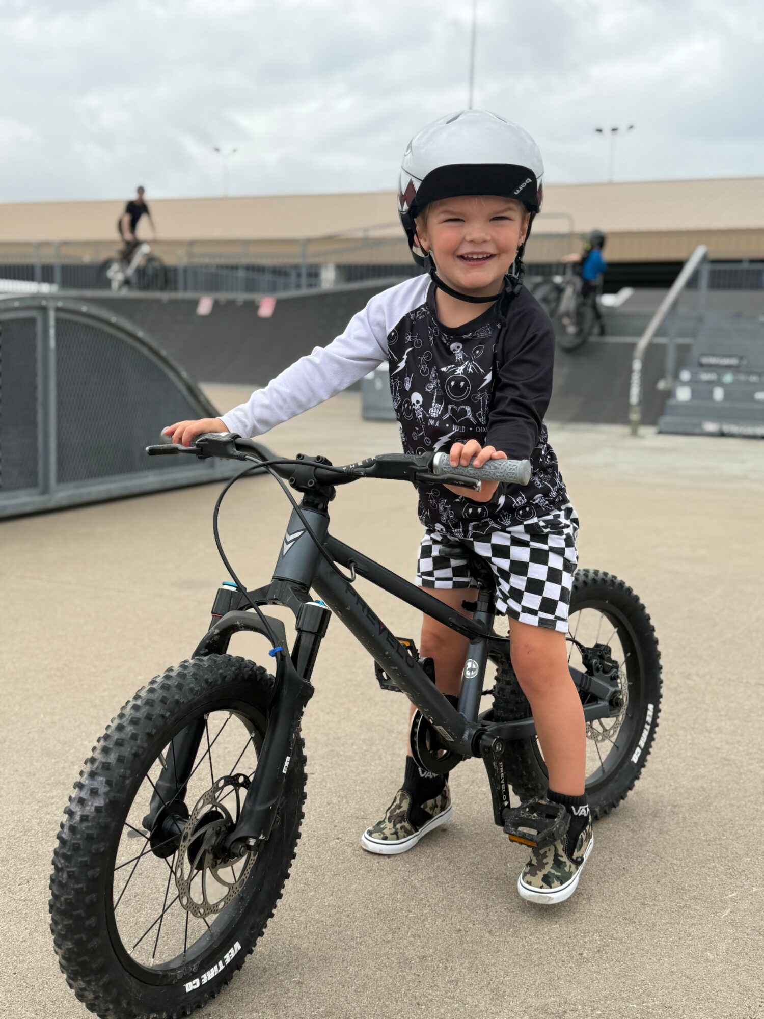 Smiling child in helmet with a mountain bike at skate park, cloudy sky background.