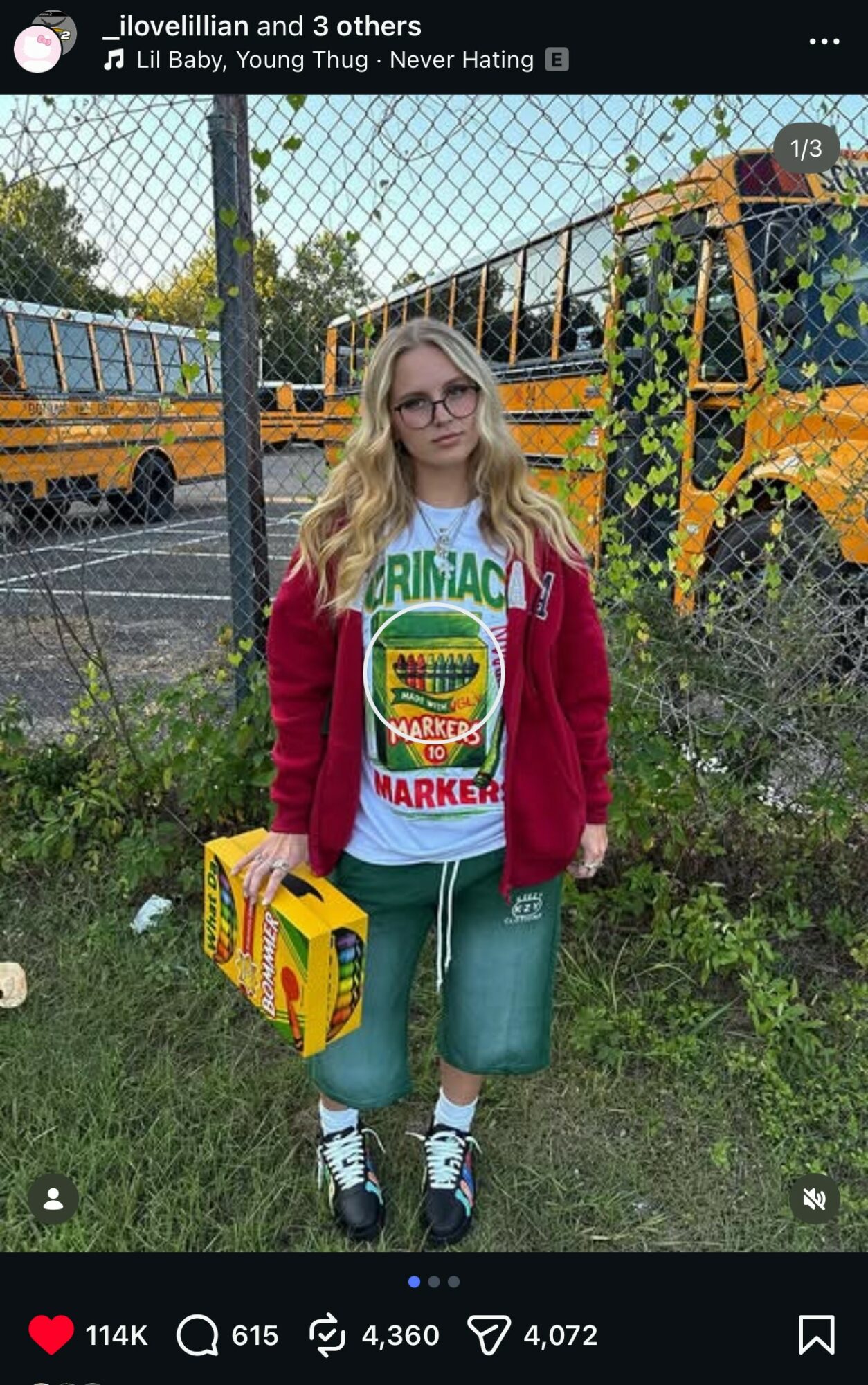 Young girl with glasses standing outdoors near a fence and yellow school buses, holding a yellow box, wearing a red jacket and graphic t-shirt.