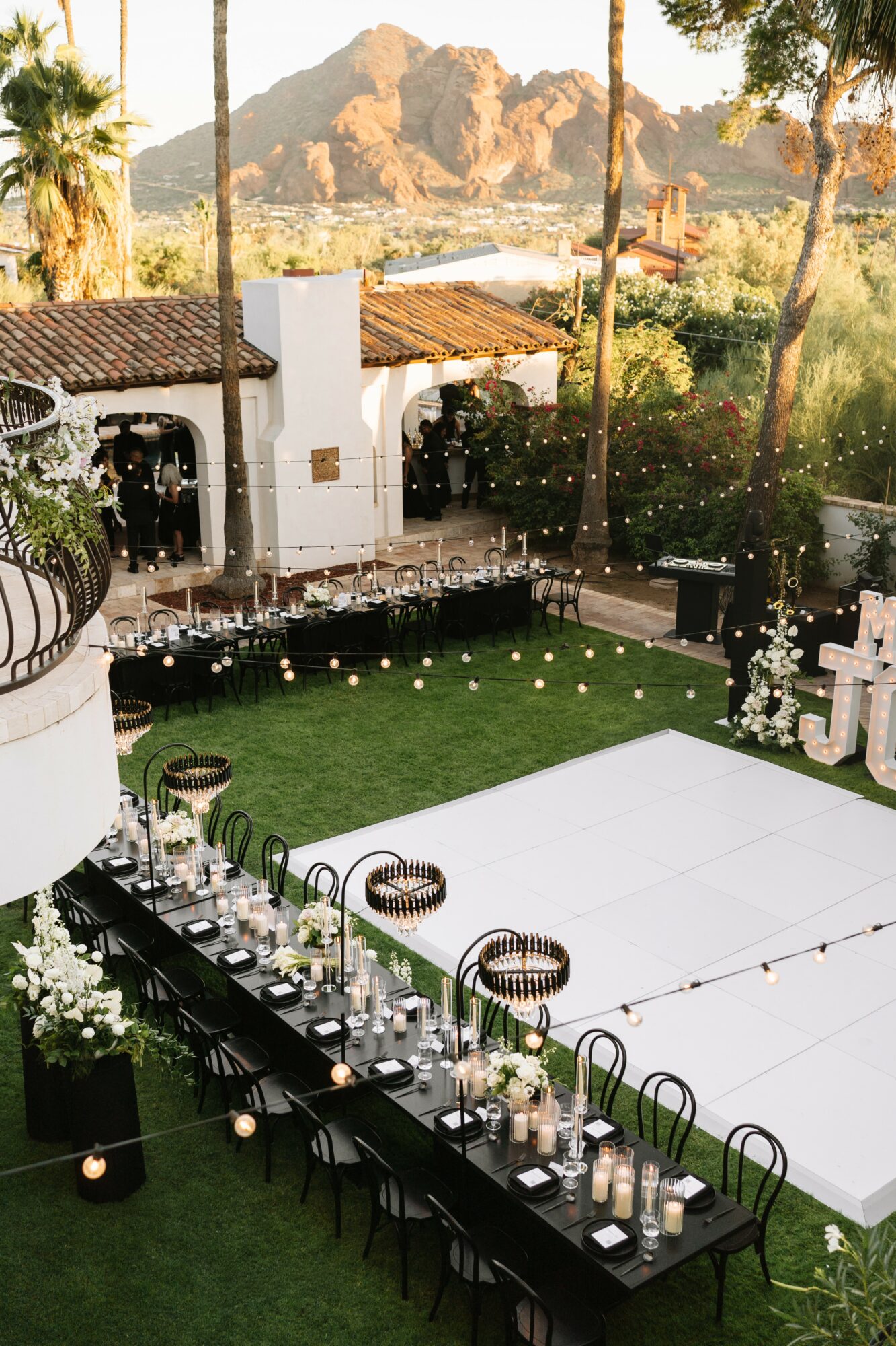 Outdoor event space with a long table, candles, and floral arrangements, surrounded by trees and mountains in the background.