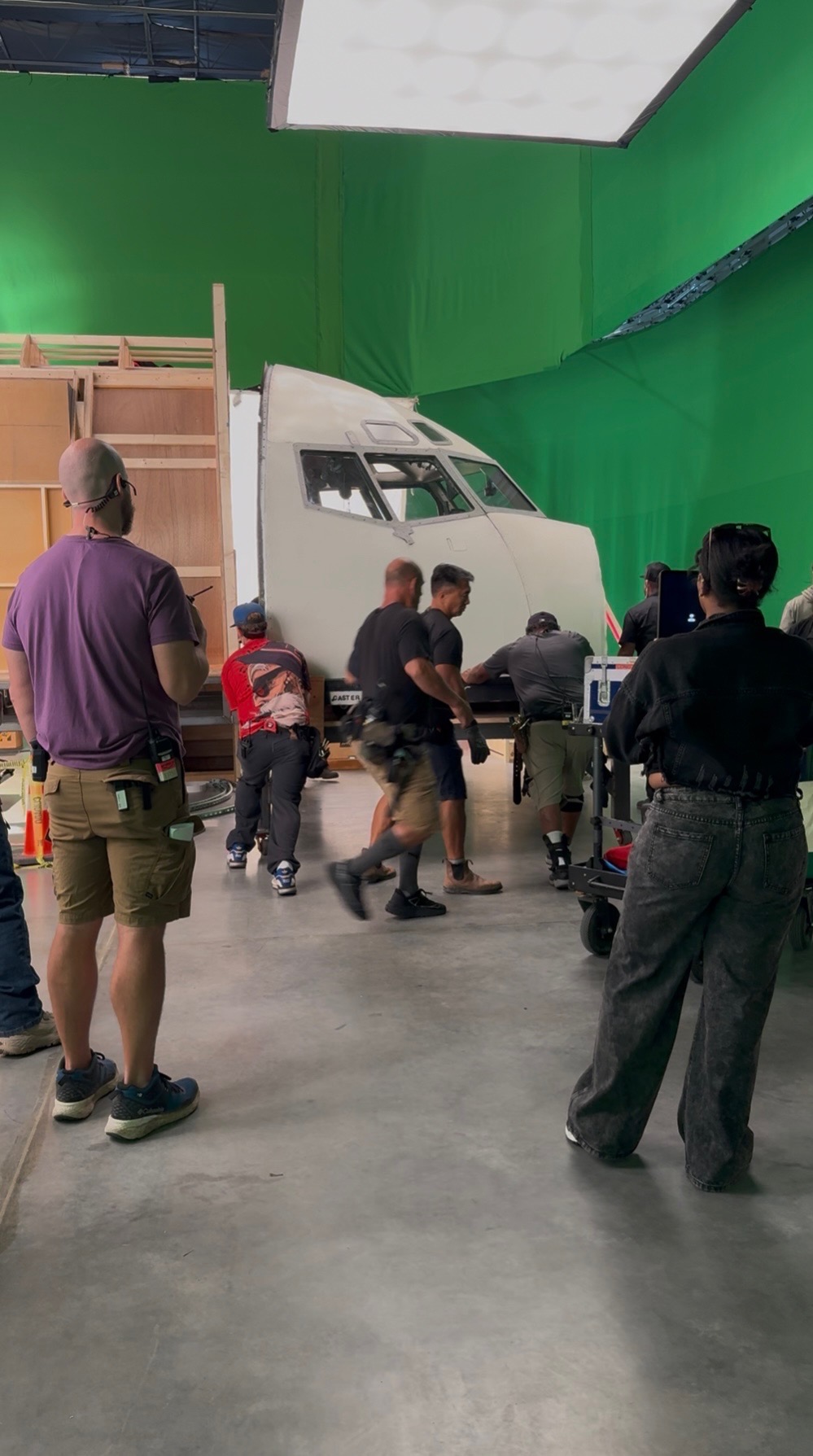 People gather around a white vehicle in a green-walled indoor space, some children and adults present.