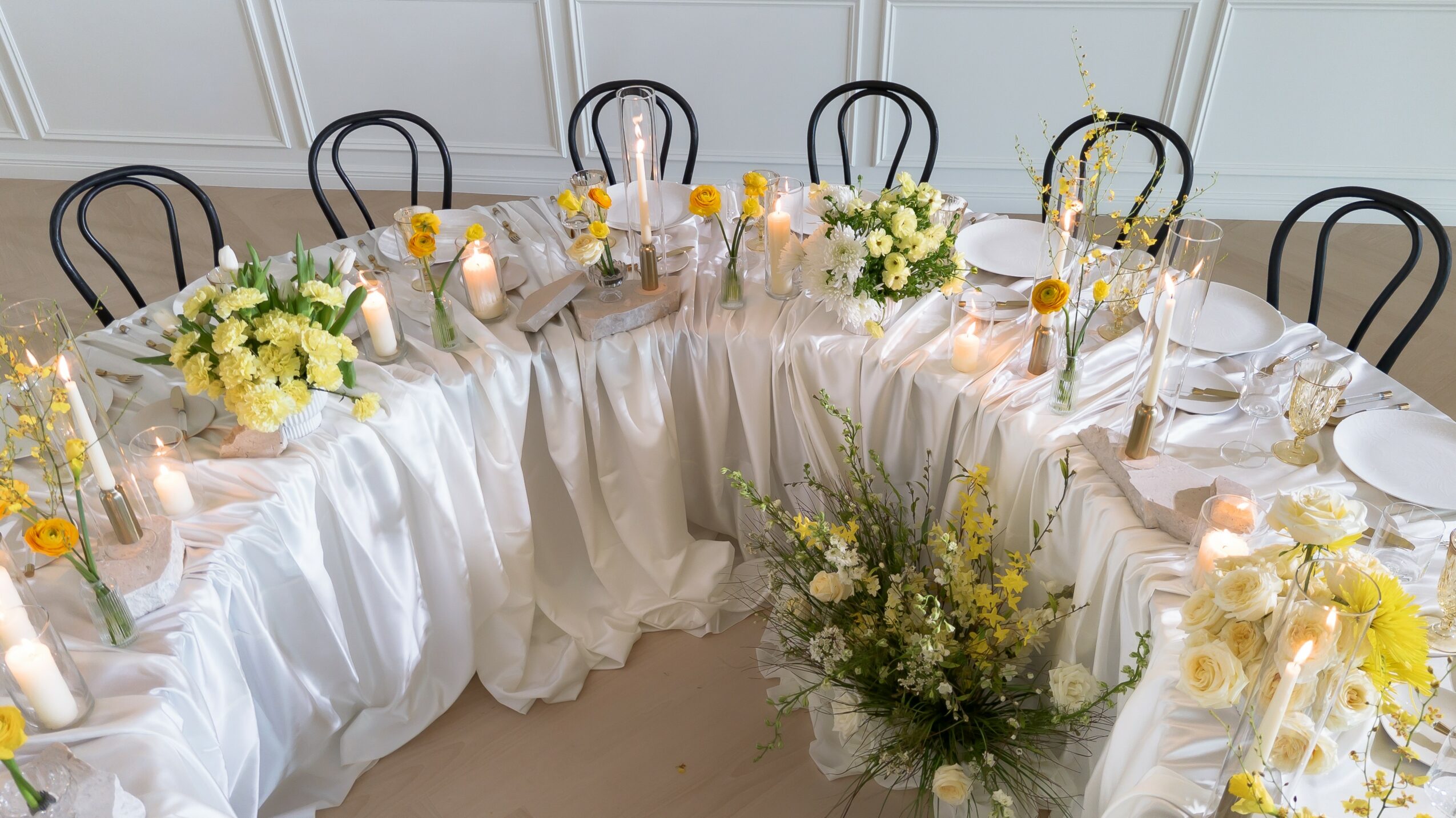 Round table decorated with white tablecloth, floral centerpieces, candles, and place settings, arranged for a formal event.