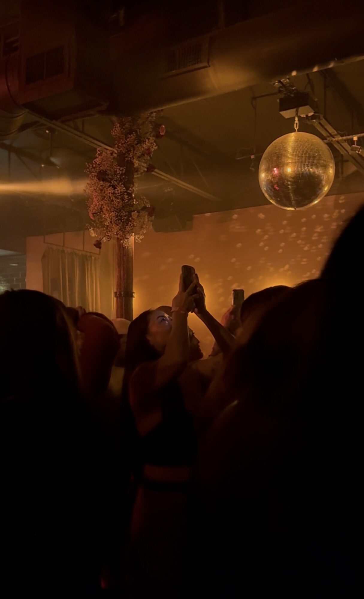 People dancing in a club with a disco ball and warm lighting, celebrating with raised hands, festive atmosphere.