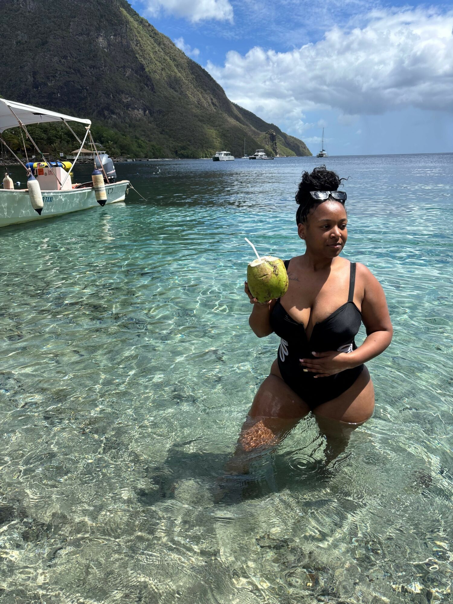Person sitting in shallow water holding a green ball, with a mountain and cloudy sky in background.