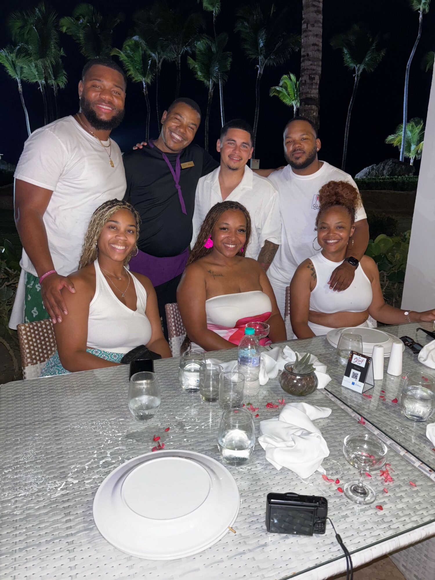 Group of six people at a table outdoors, with drinks and plates, smiling and posing for the photo.