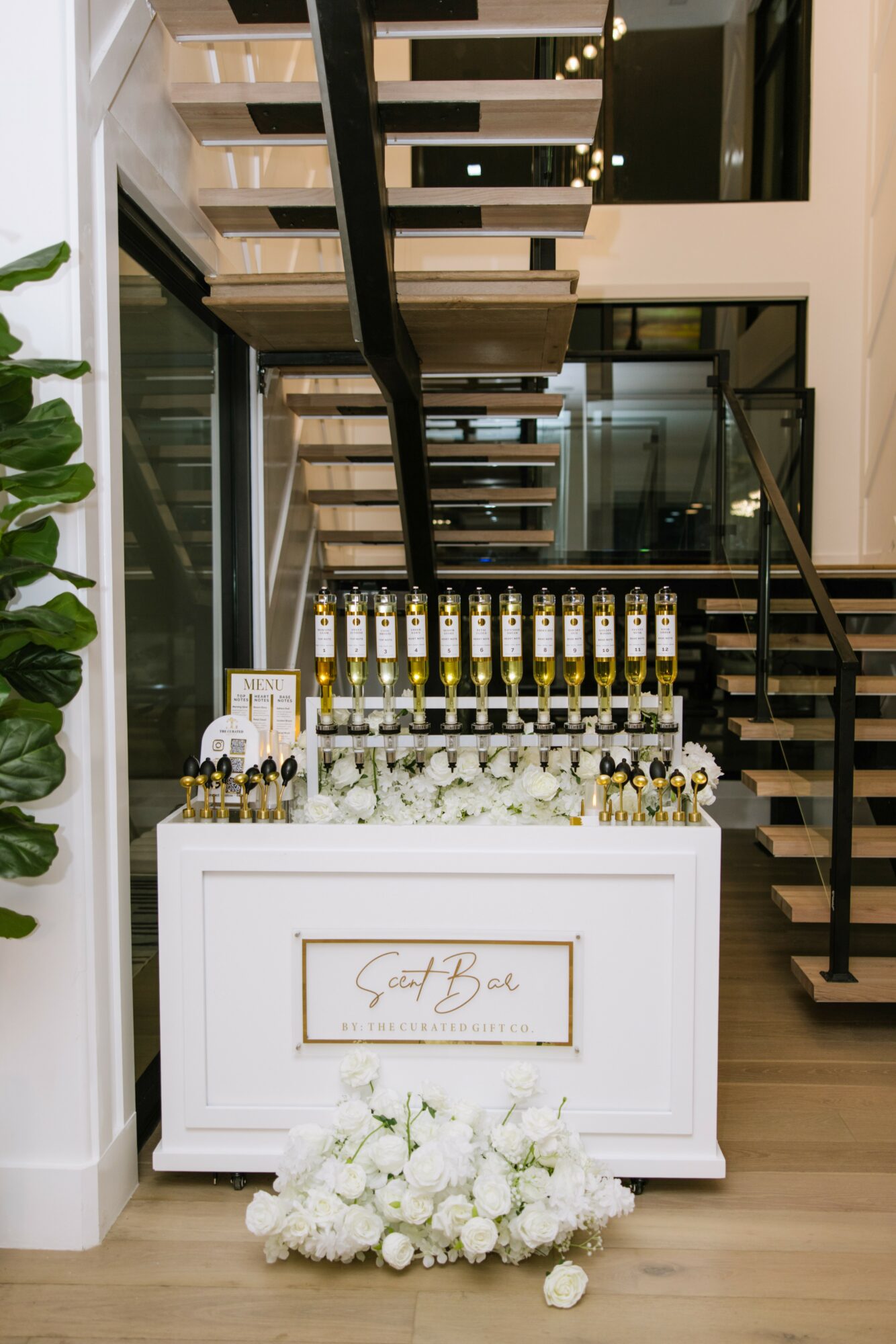 A white table with bottles and flowers, decorated with white flowers at the base, in a modern interior setting.