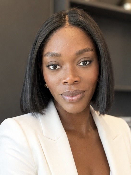 Portrait of a woman with straight black hair, wearing a white blazer, looking at the camera with a neutral expression.