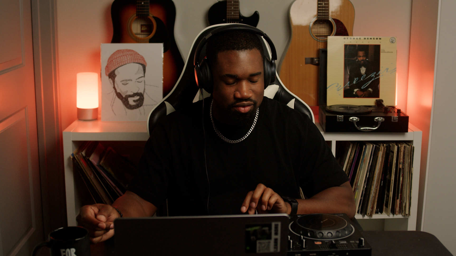 Person wearing headphones using DJ equipment in a room with guitars and artwork, warm lighting, and vinyl records.