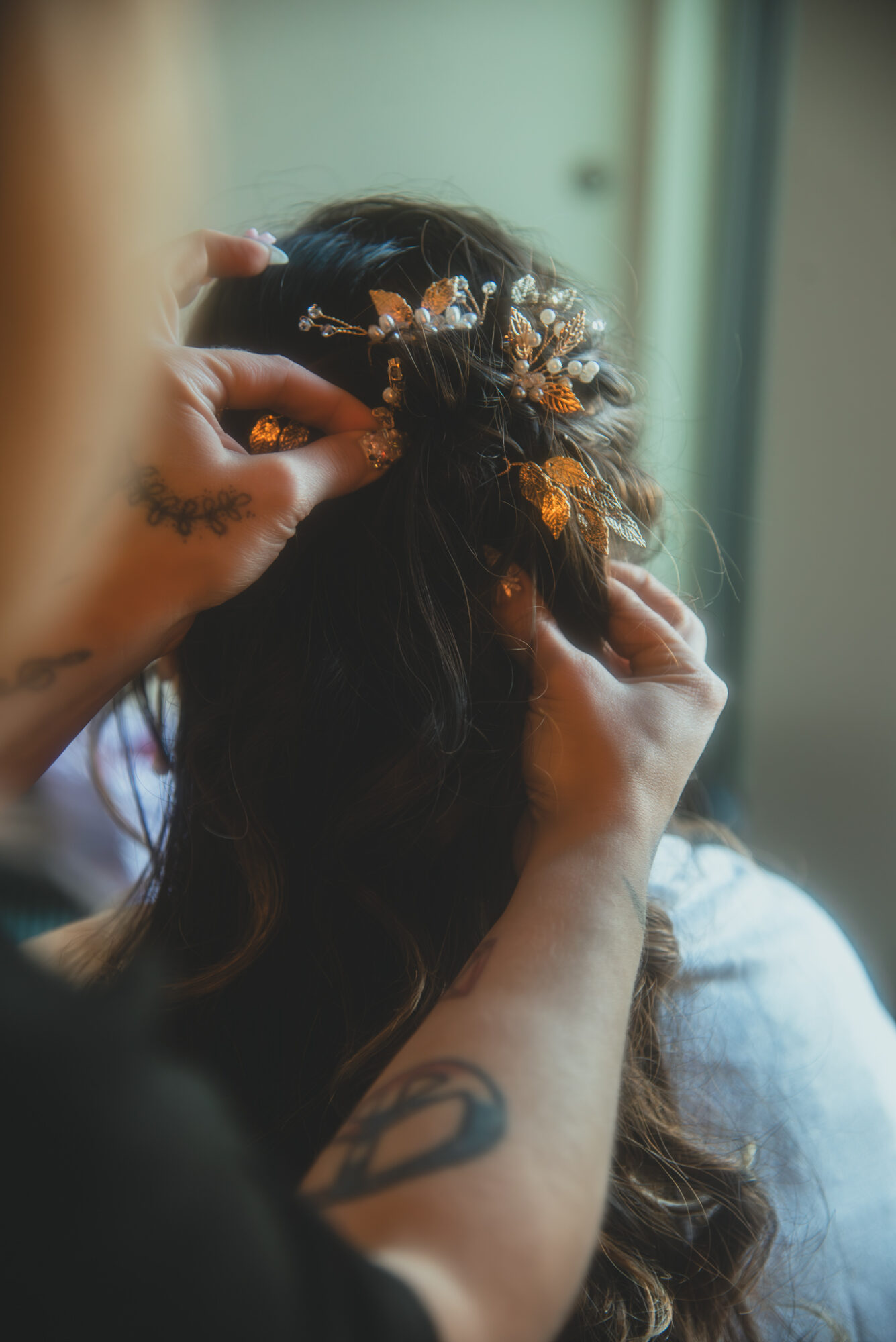 Person styling a woman's hair with decorative accessories, focus on hands and hair, background blurred.