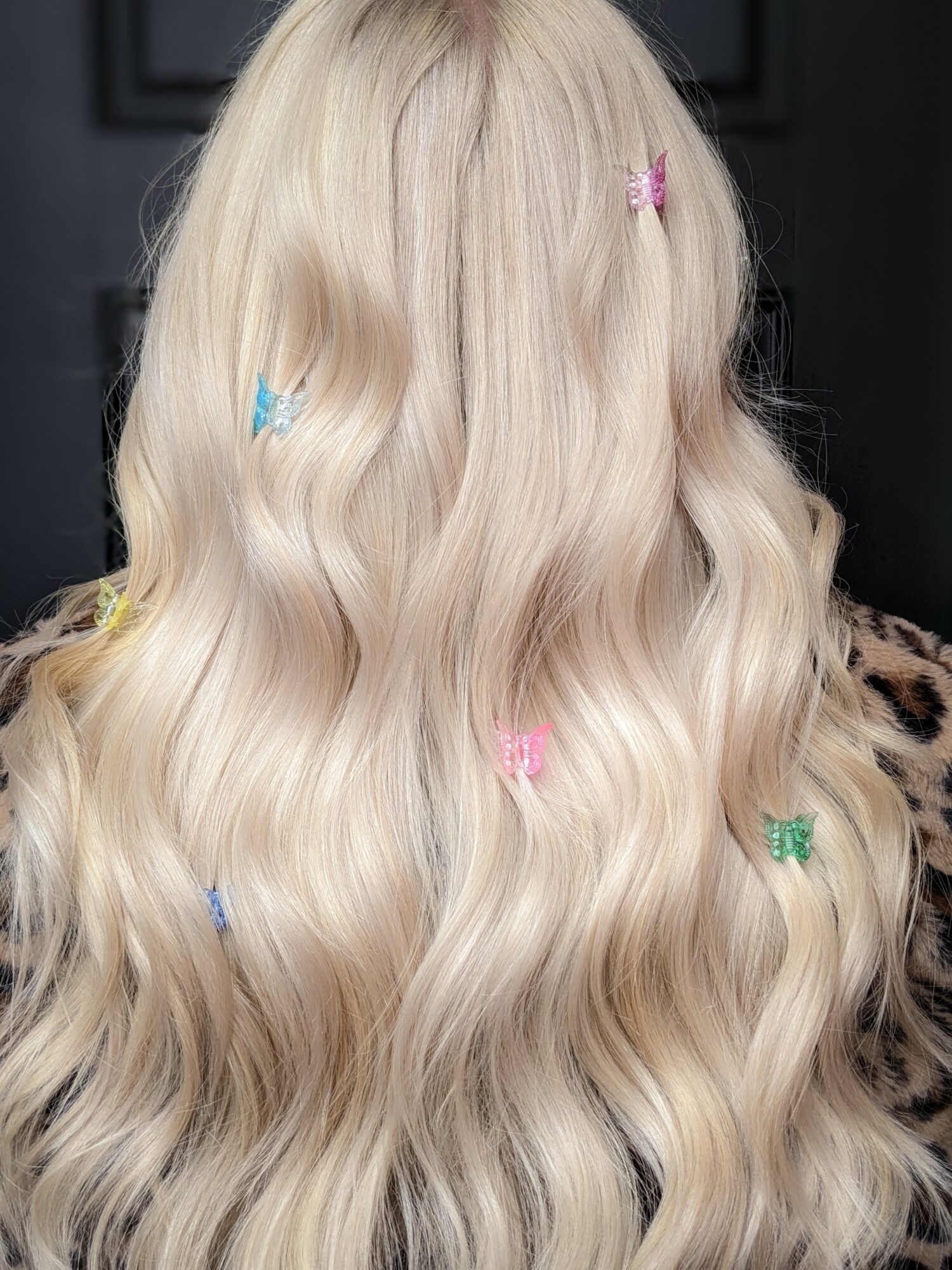 Back of a person with long, wavy, platinum blonde hair decorated with small colorful hair clips.