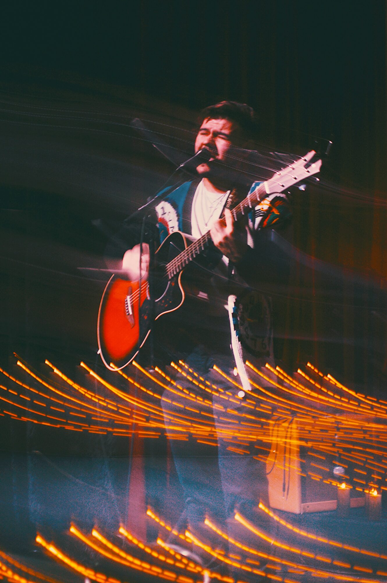 Person playing guitar on stage with colorful lights and dark background.