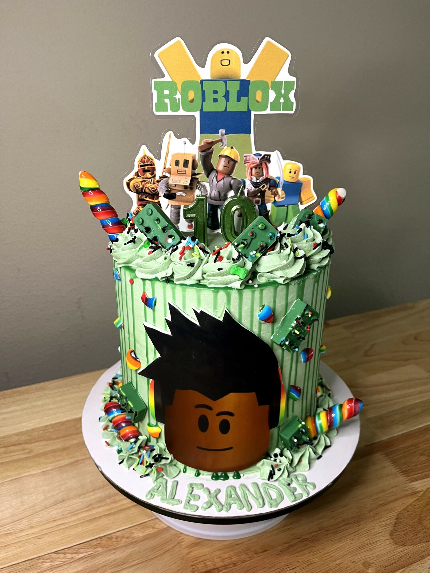 Roblox-themed birthday cake with character toppers, green frosting, and colorful decorations, on a wooden surface.