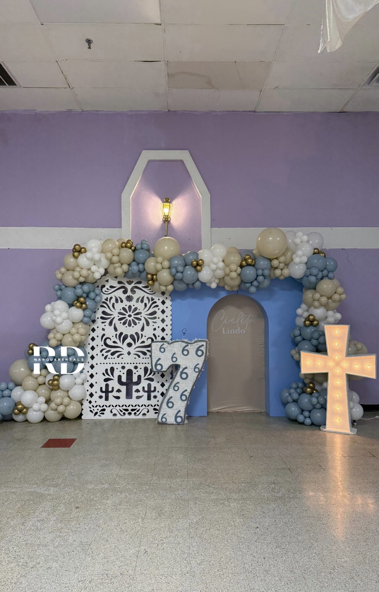 Decorative arch with balloons, a cross, and a patterned panel in a room with purple walls, ceiling, and a light fixture.