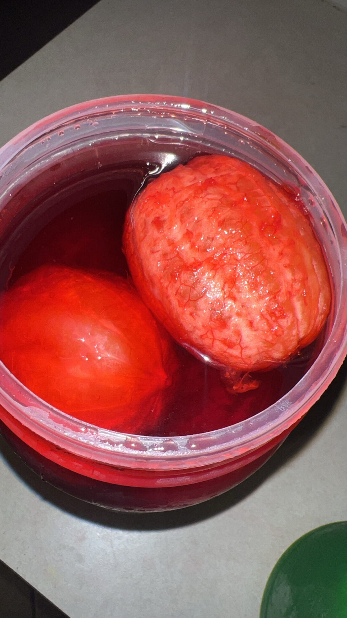 Two red apples inside a transparent container with a red lid, placed on a gray surface.