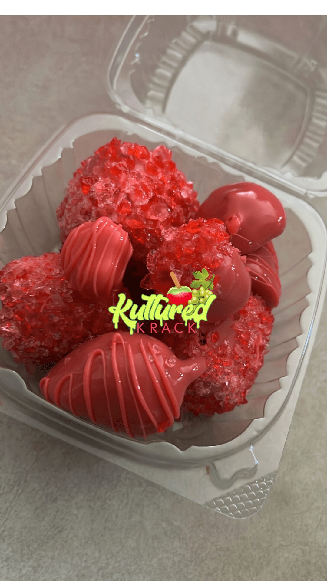 Container with red, coated strawberries and berries, some with chocolate drizzle, on a clear plastic lid.