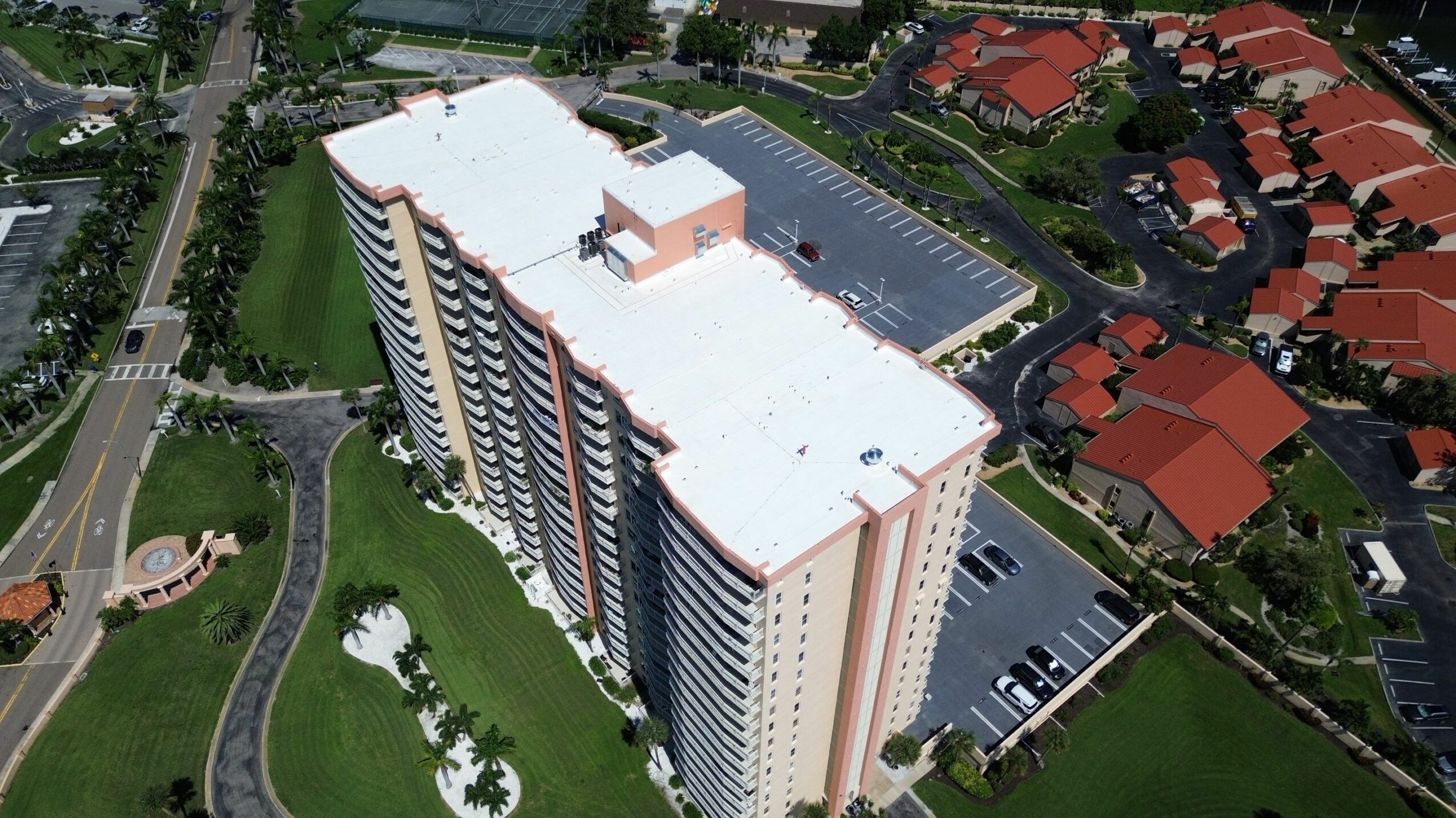 A tall, multi-story building with a white roof, surrounded by parking lots and residential houses, seen from above.