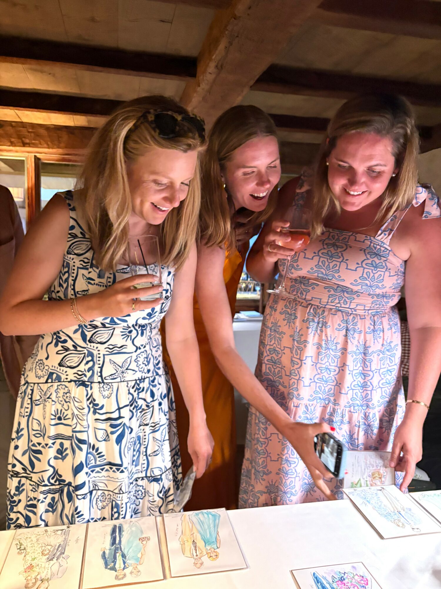 Three women smiling and looking at colorful drawings on paper on a table indoors.