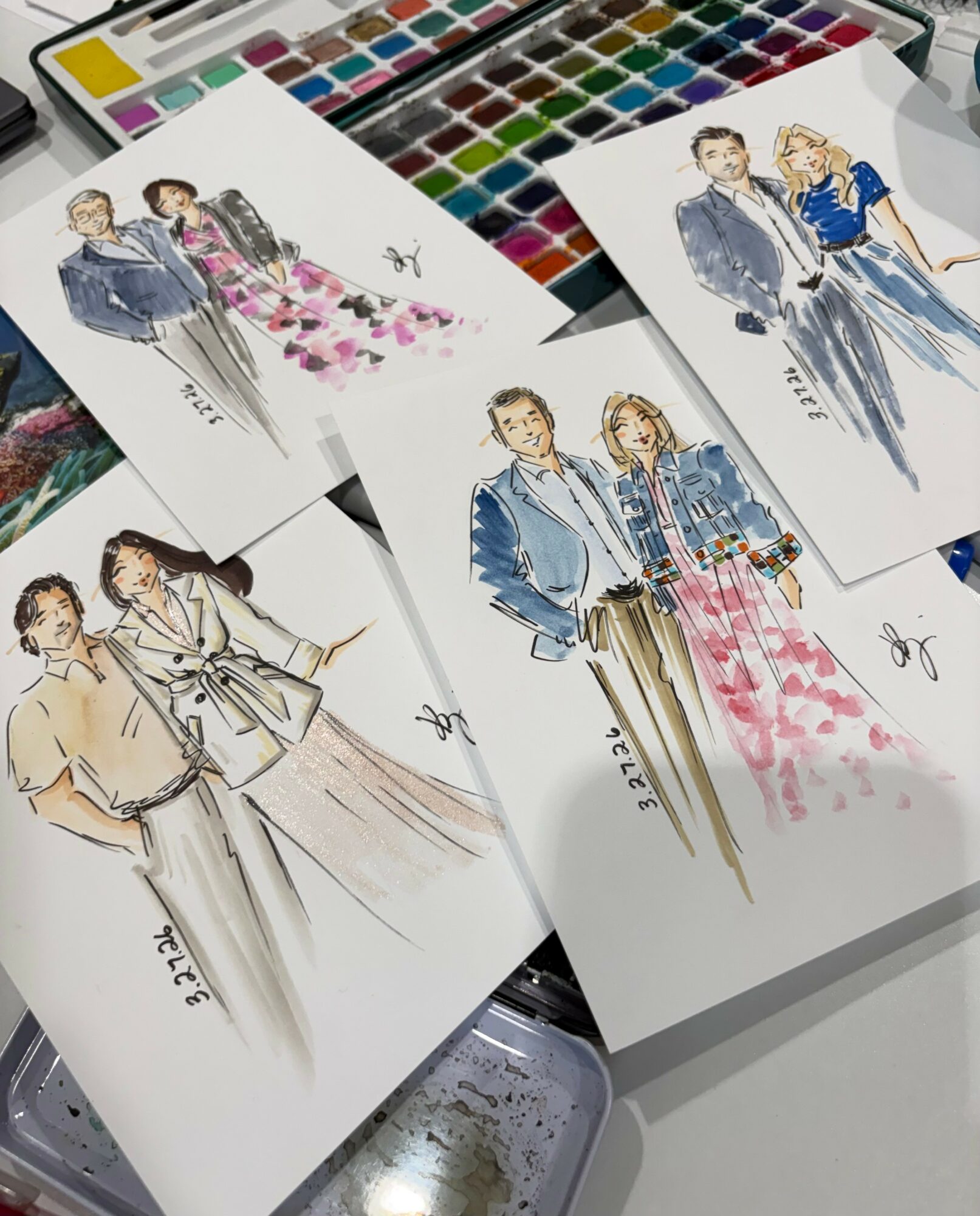 Fashion illustrations of people in stylish clothing, with watercolor effects, on white paper, surrounded by watercolor paints and brushes.