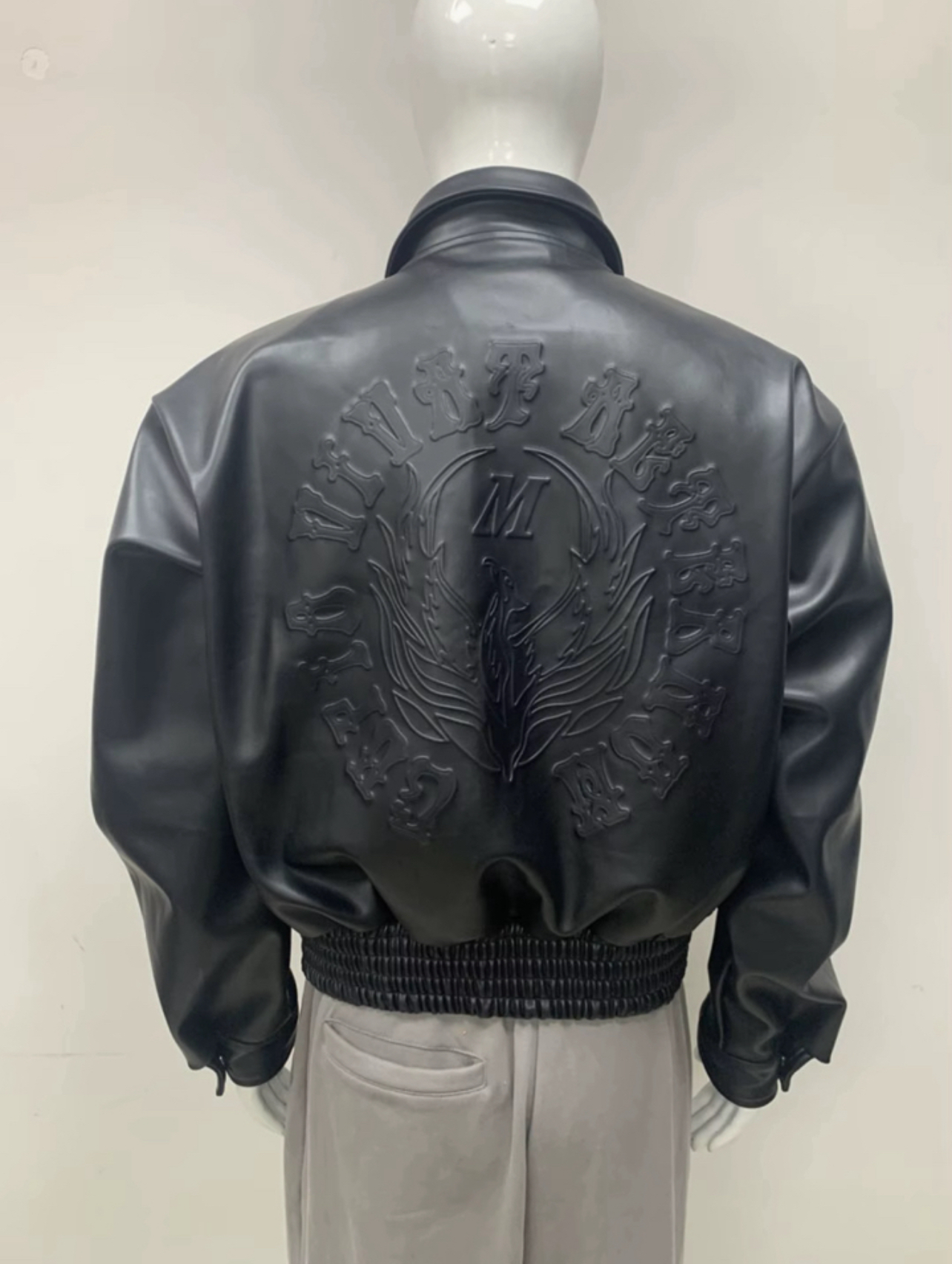 Mannequin wearing a black leather jacket with embossed design on the back, standing against a plain background.