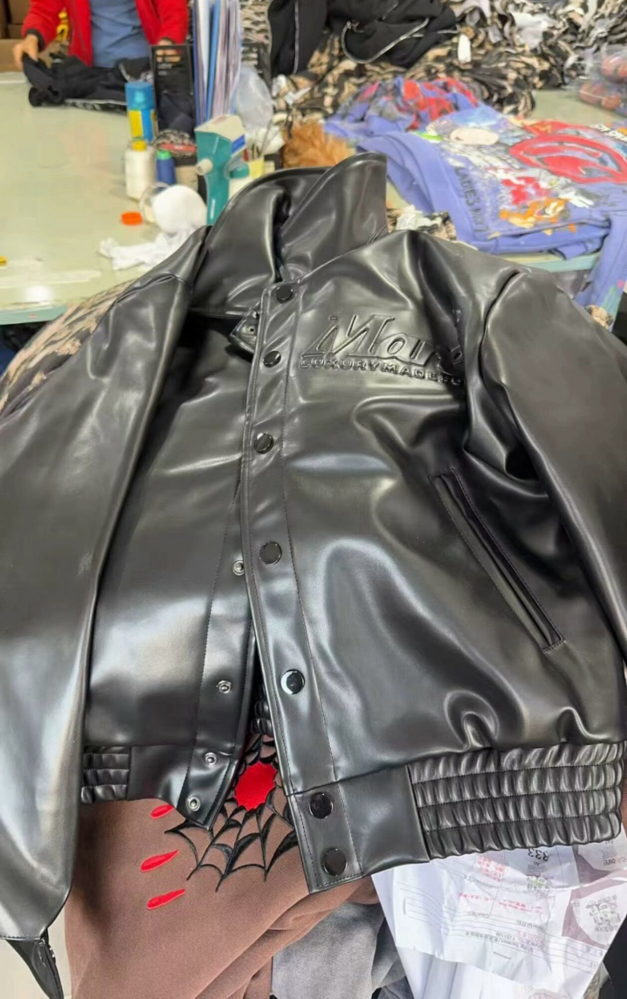 Black leather jacket draped over a surface with various items and clothing in the background.