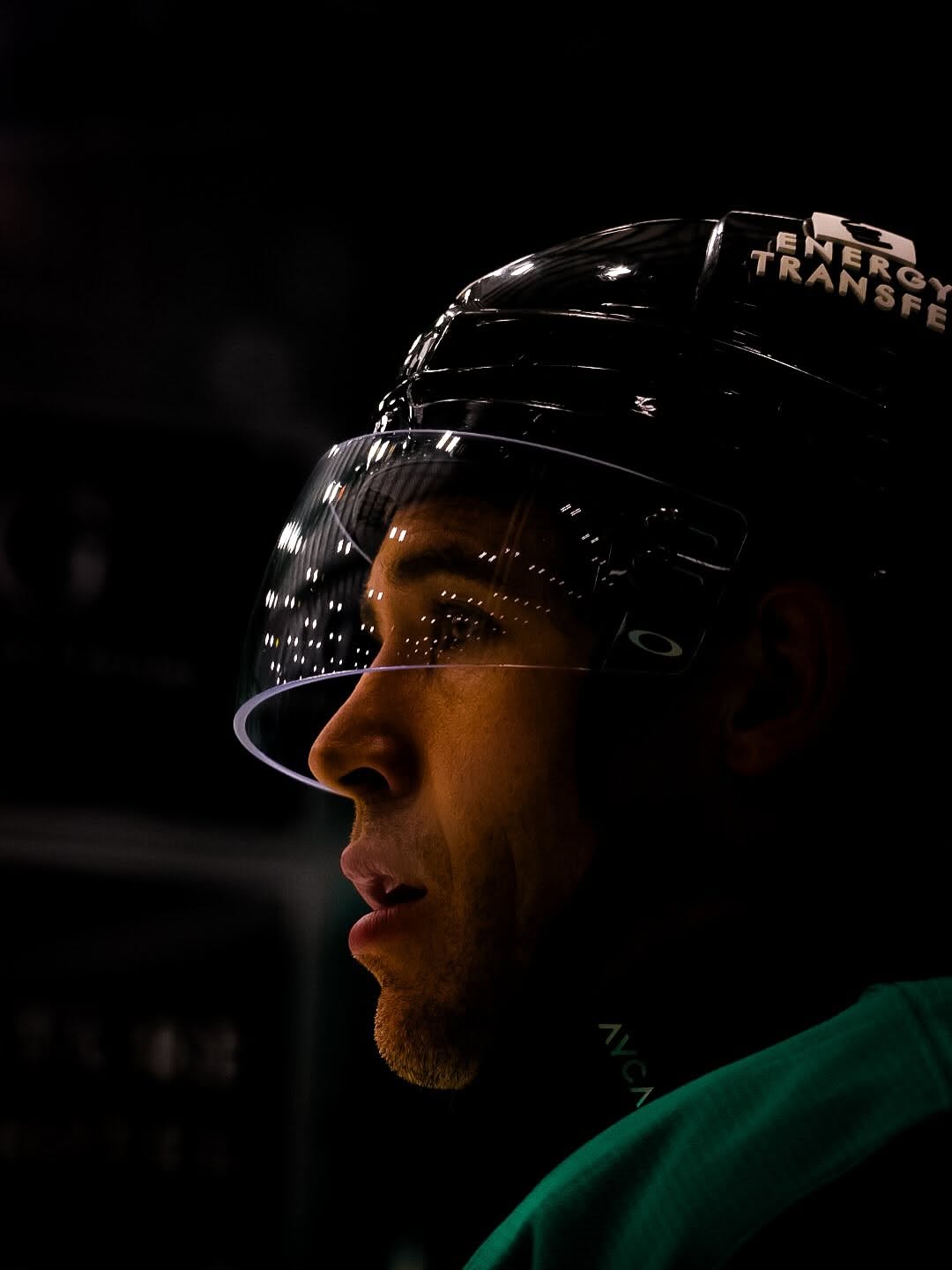 Close-up profile of a person wearing a helmet, with a dark background, illuminated by a light source highlighting facial features.