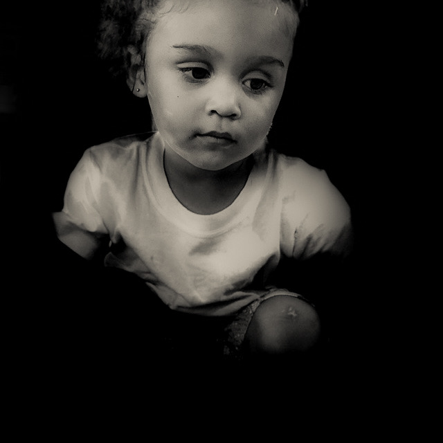 Child with curly hair looking down, wearing a light-colored shirt, in black and white.
