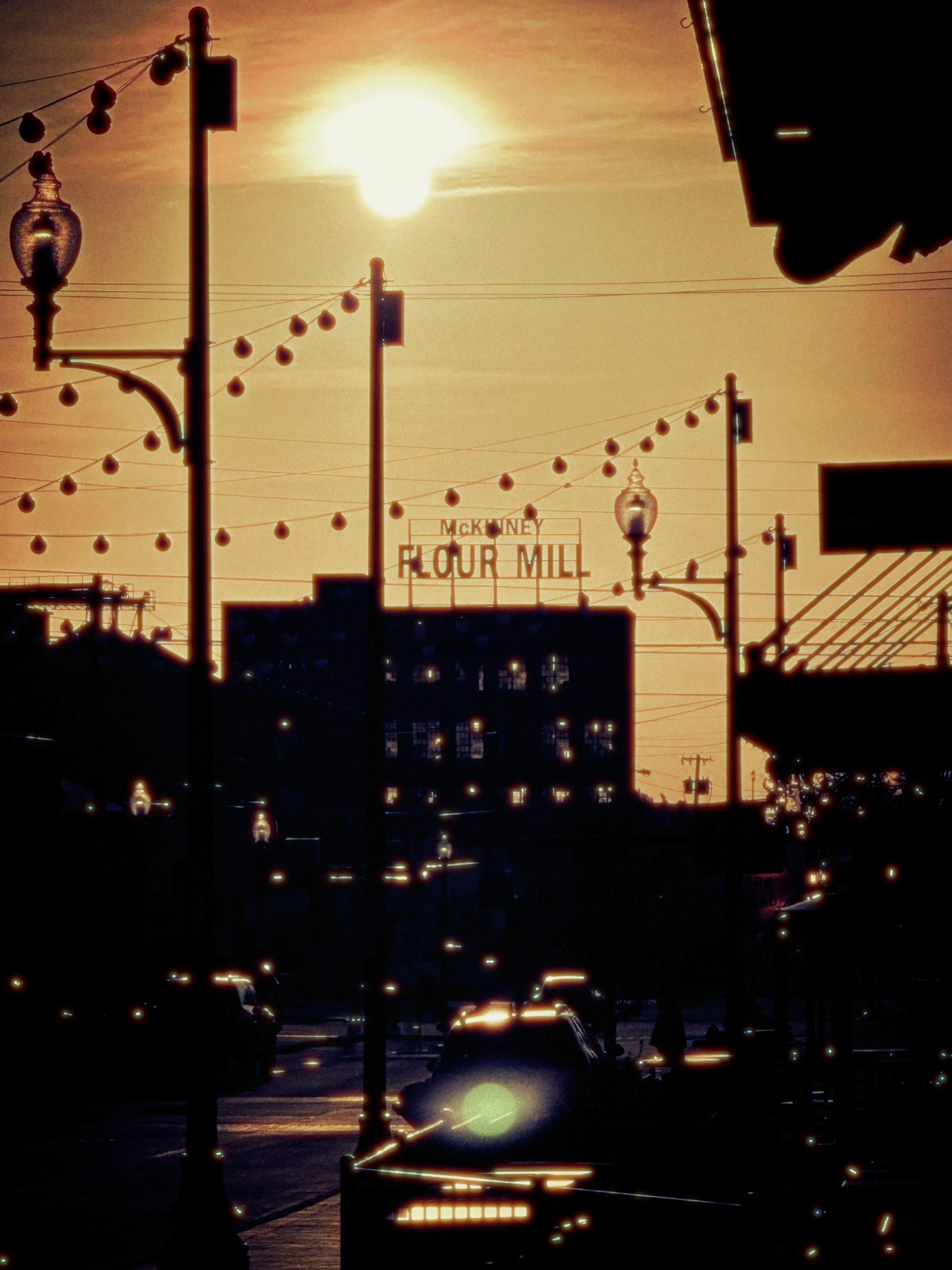 Sunset over a city street with streetlights, power lines, and a building with a sign reading 'FLOUR MILL'.