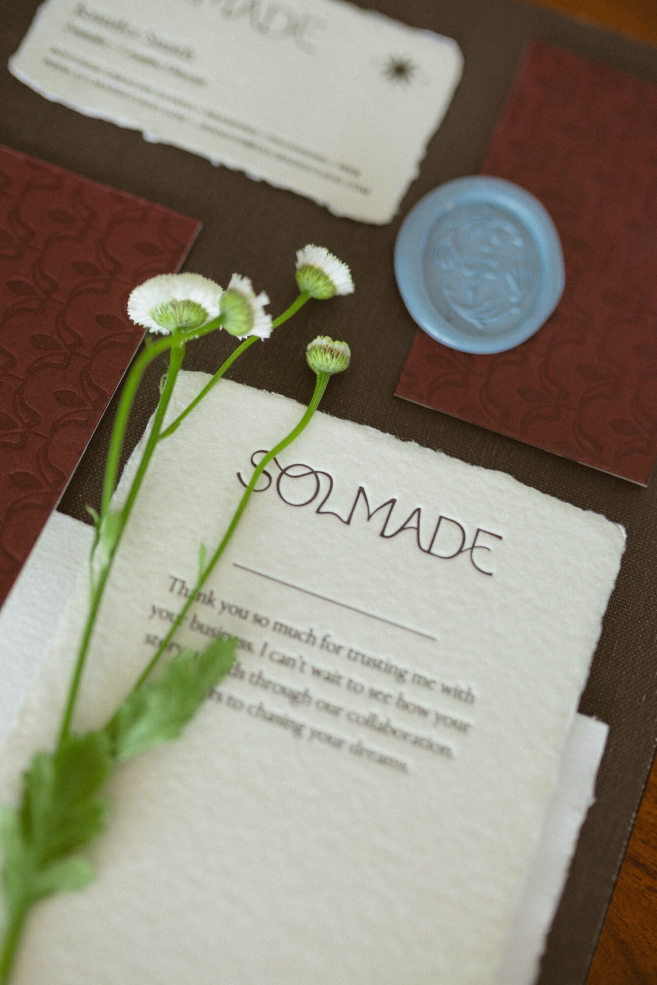 White paper with handwritten word 'GOMADE' and a blue wax seal, with white flowers in the foreground.