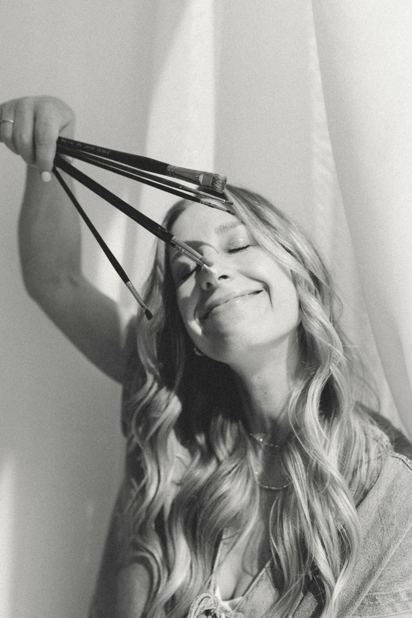 Woman smiling with eyes closed, holding a headband with multiple straps above her head.
