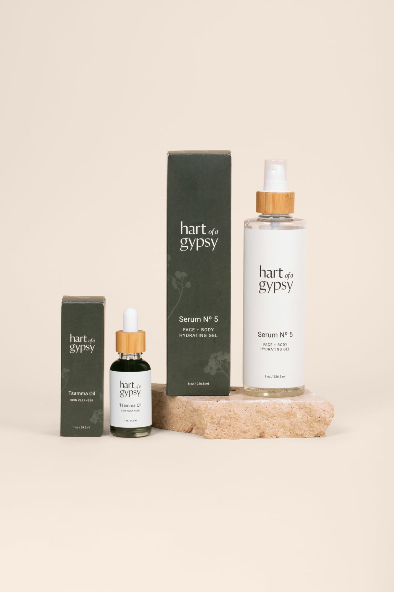Three skincare bottles and boxes arranged on a beige surface against a light background, with one bottle on a small stone slab.