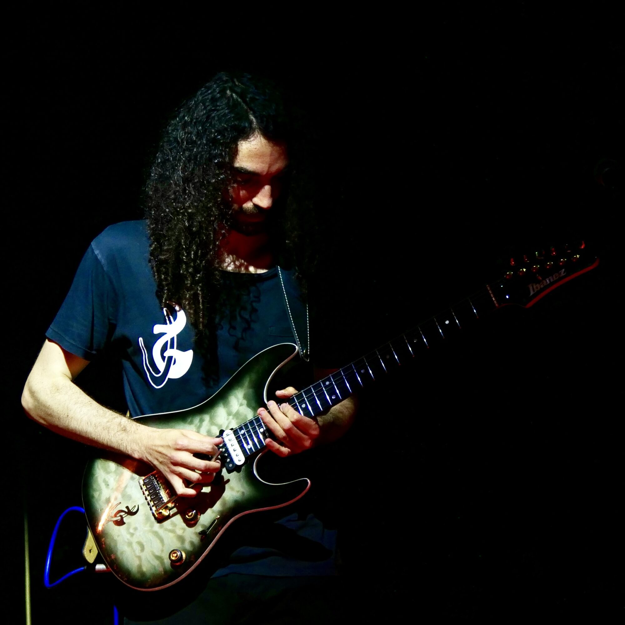 Person with curly hair playing an electric guitar on a dark background.