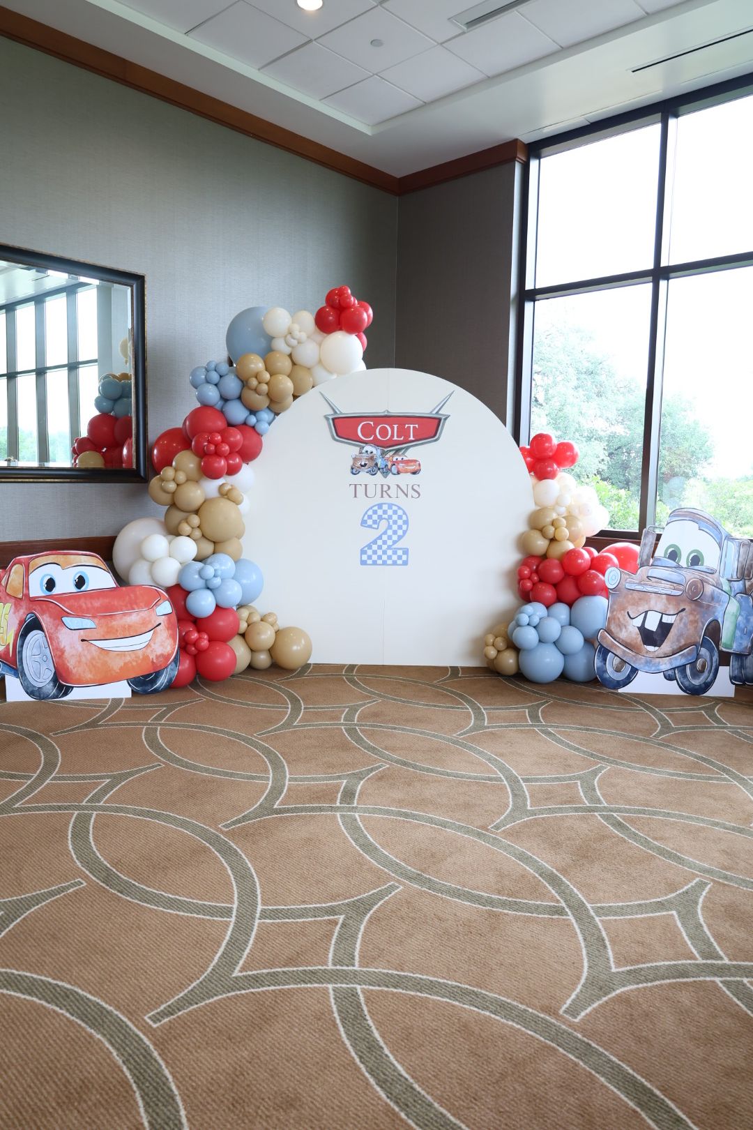 Decorative display with balloons and a sign, featuring a cartoon character, in front of large windows and a tiled floor.