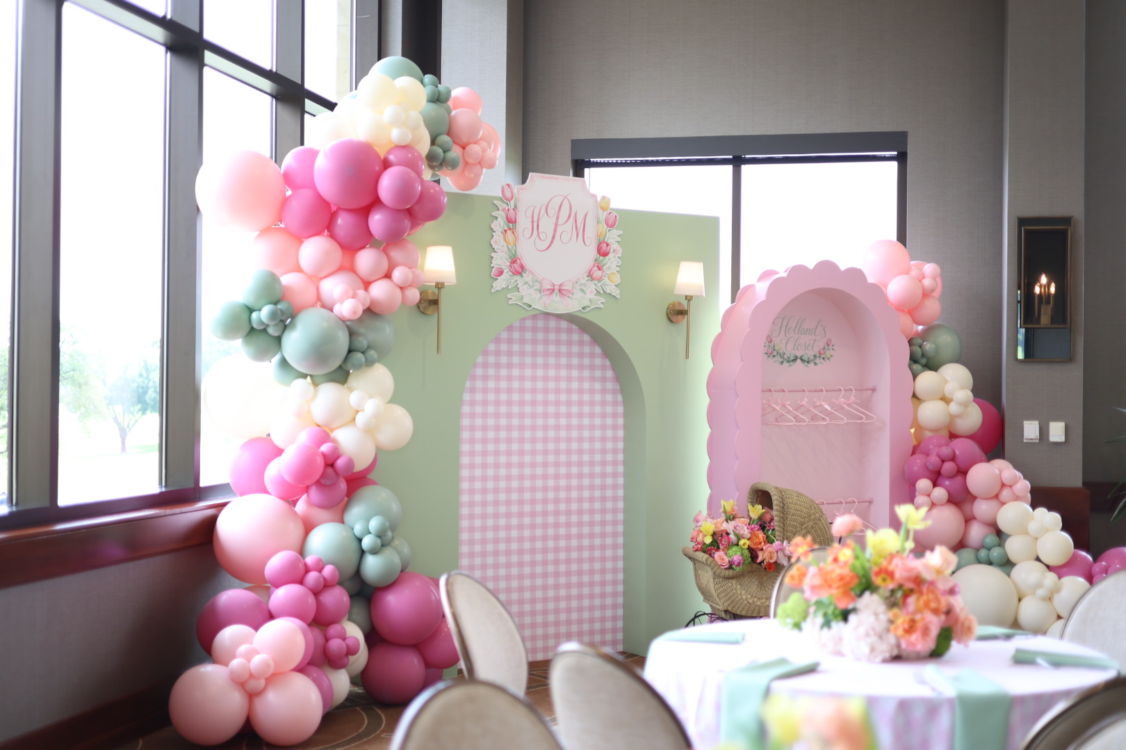 Decorative balloon arch with pink, white, and pastel colors surrounds a pink and white backdrop with floral arrangements.