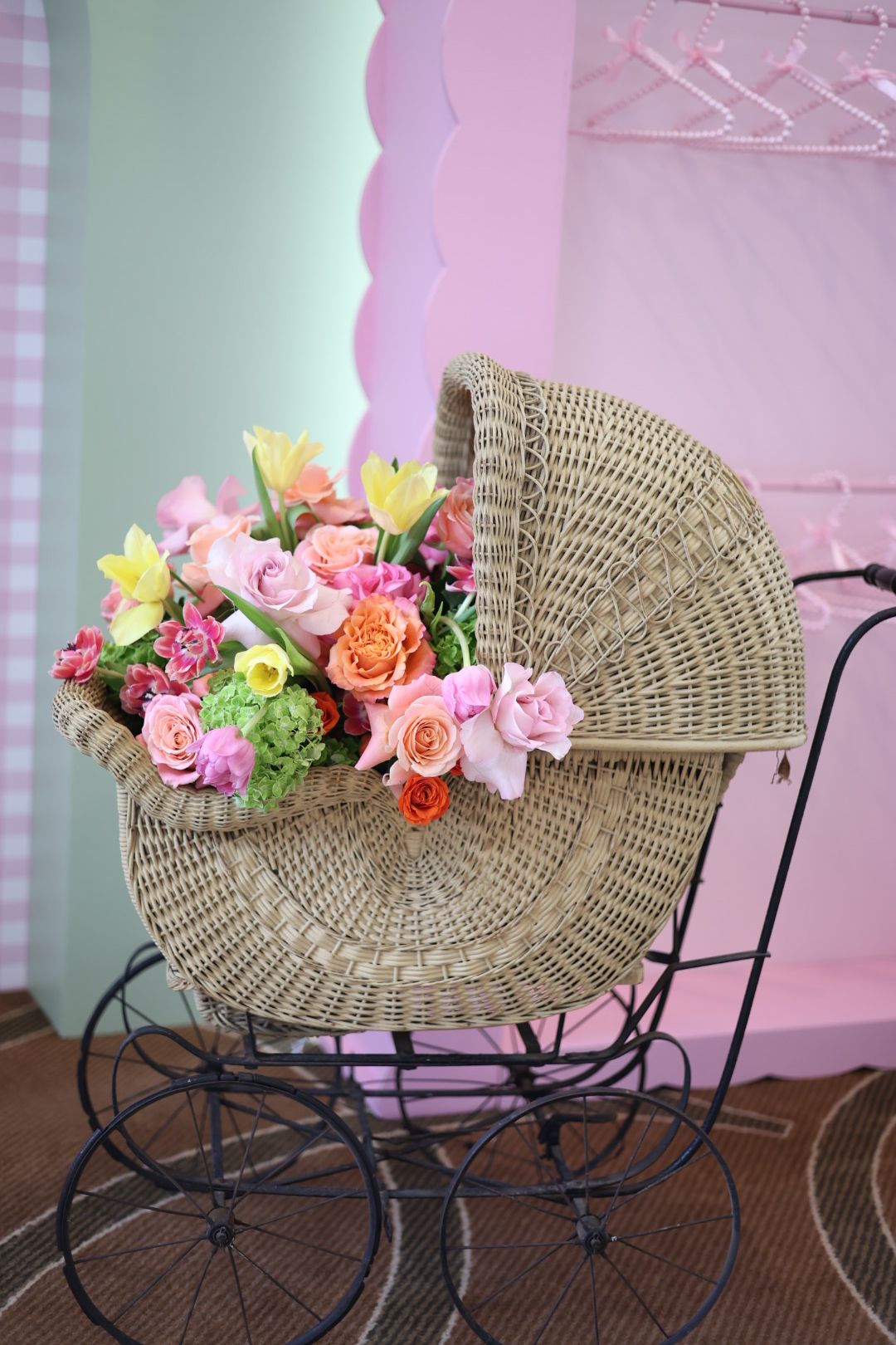 Wicker handbag with pink, yellow, and orange flowers on a black metal chair, pink and green background.