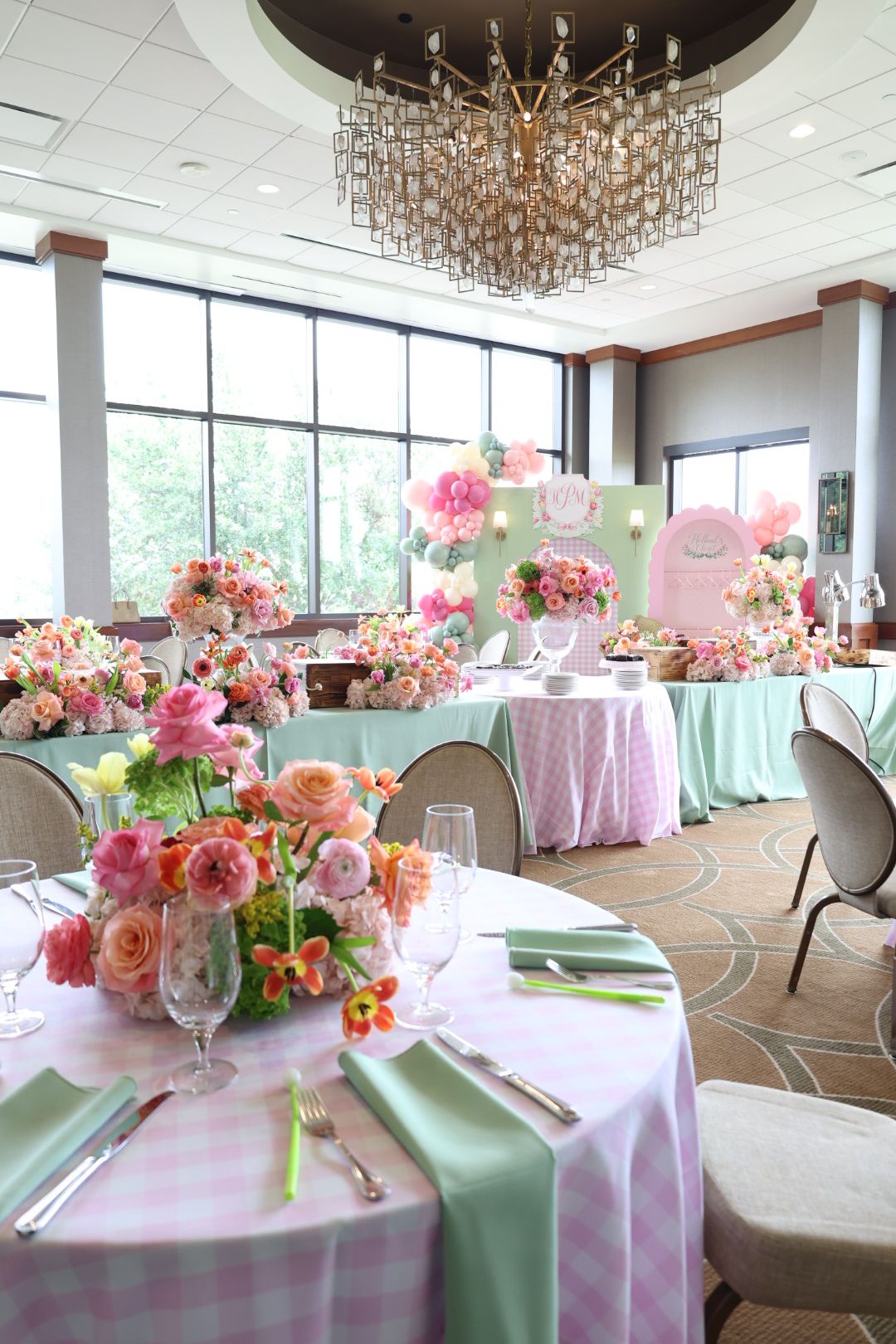 Elegant table setup with pink and peach floral arrangements, pink tablecloth, and chairs with pastel covers in a bright room.