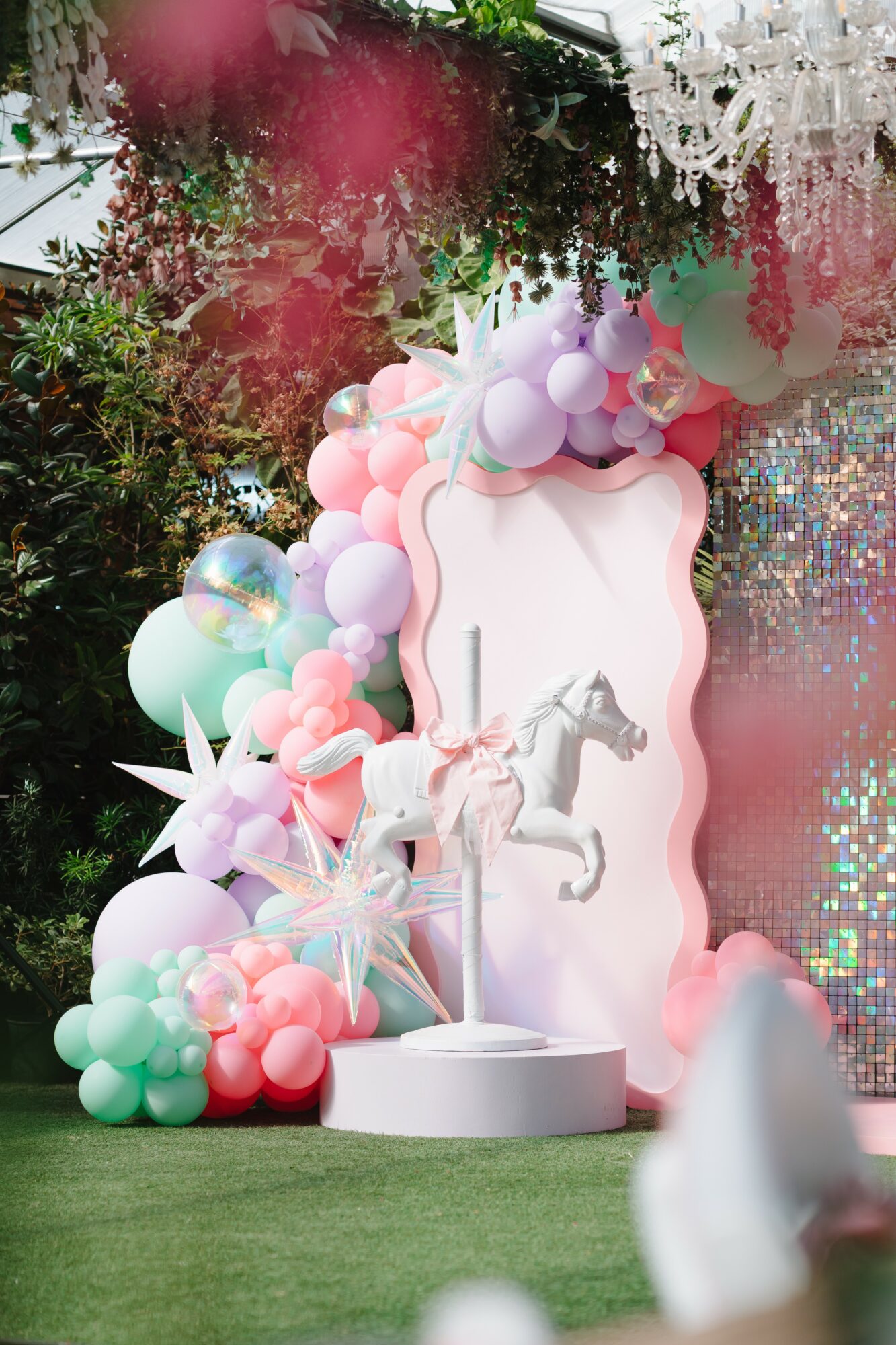 Decorative setup with pastel balloons, unicorn figures, and a pink and white backdrop, resembling a whimsical scene.