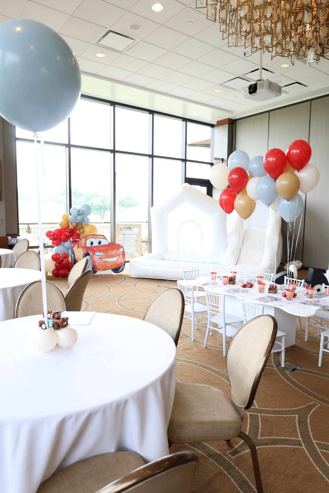 Party table with balloons, drinks, and decorations in a bright room with large windows.