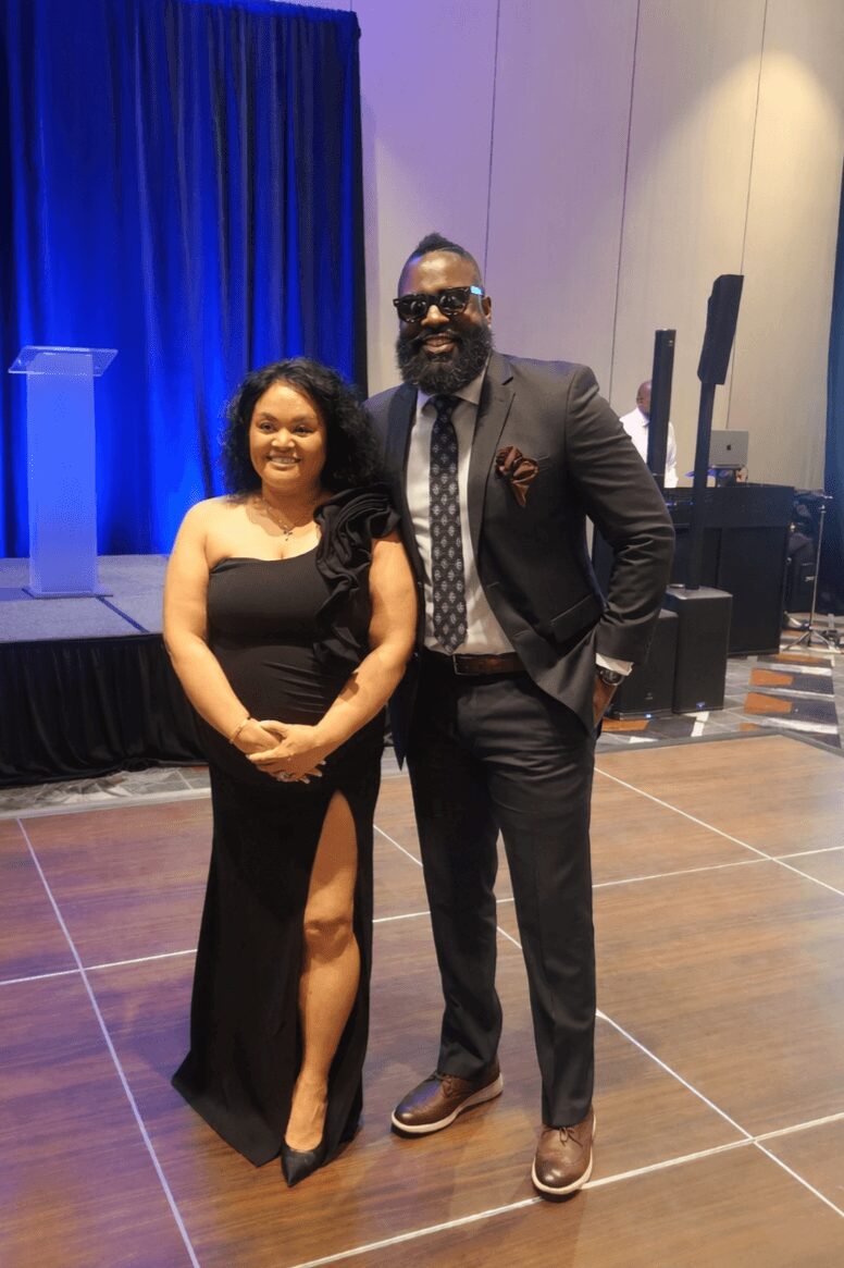 A woman and a man in formal attire standing together on a stage, smiling at the camera.